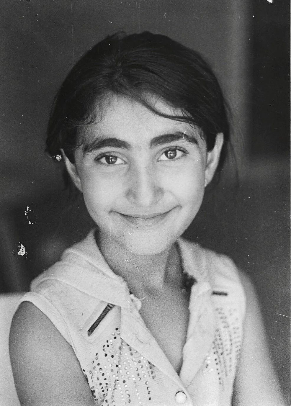 Black and white portrait of young girl with short dark hair, smiling, wearing a sleeveless top with embellishments.