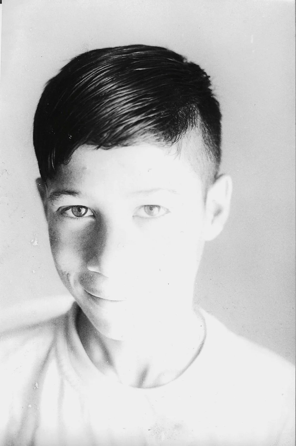 Black-and-white portrait of a young person with short, slicked-back hair and light-colored eyes, wearing a light-colored shirt.