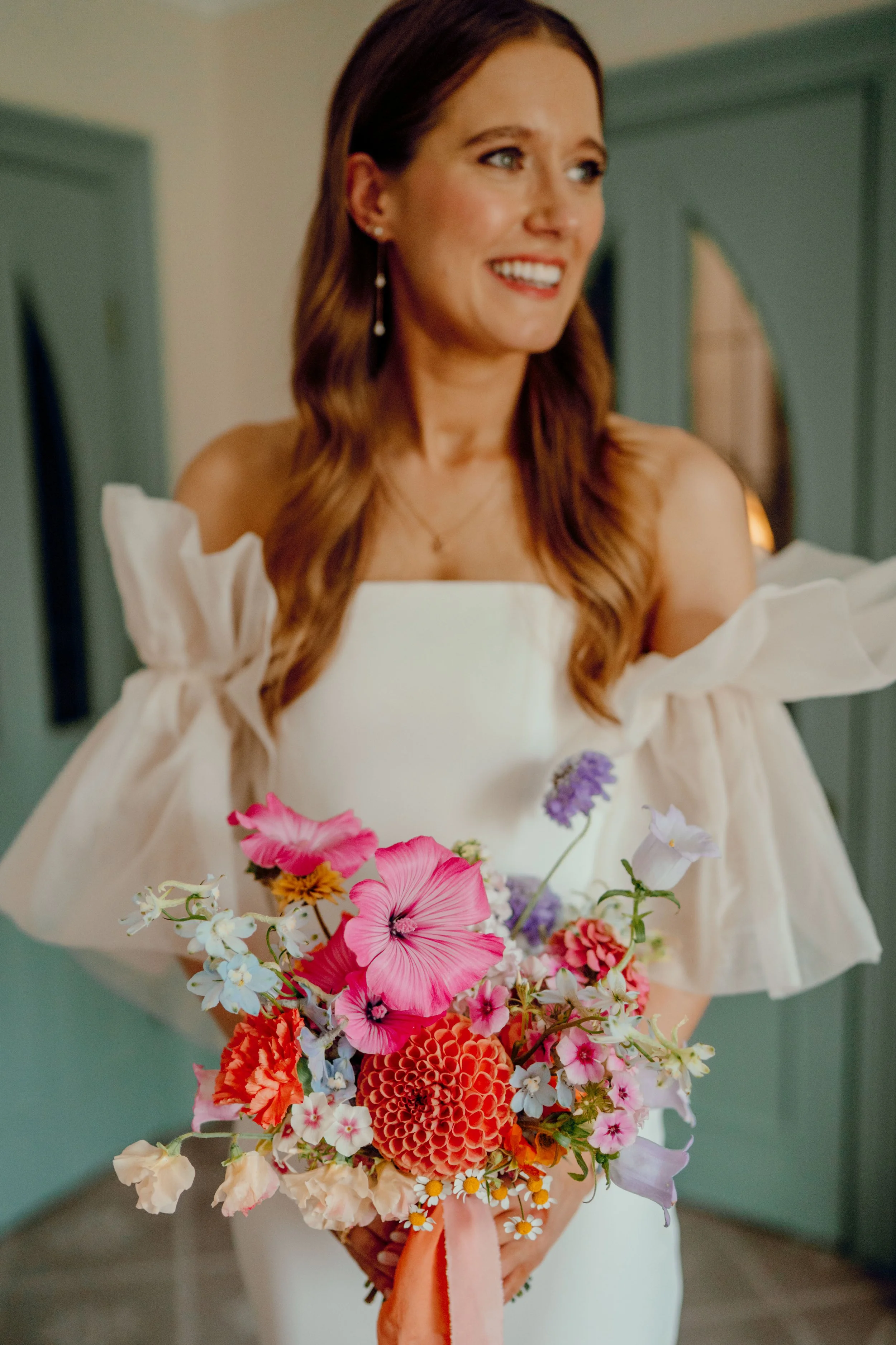 A young happy bride ready to get married holding her bright, modern bridal bouquet in oranges, pinks, delphinium blue, and lilac