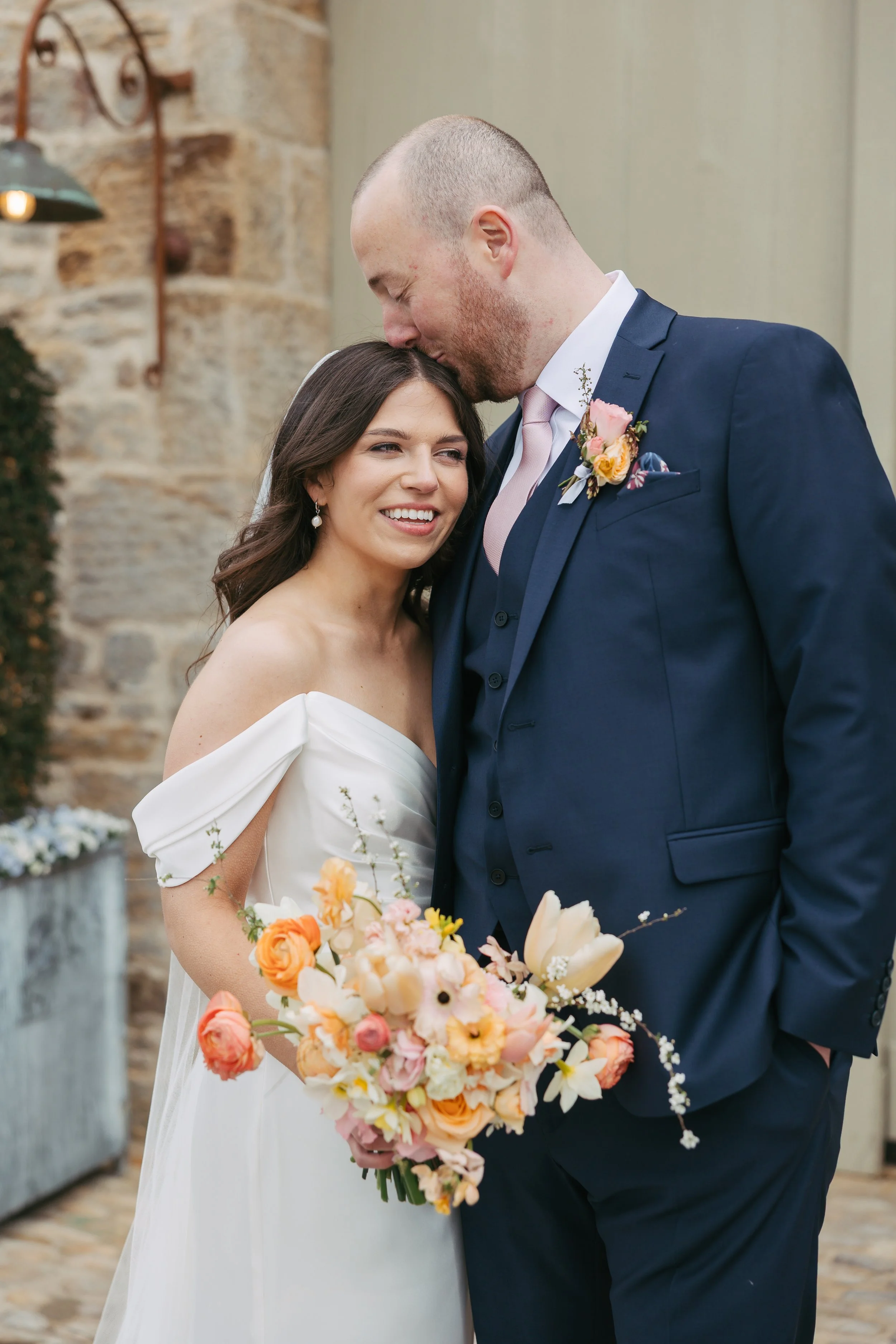 Bride and groom just married outside The Tithe Barn, Bolton Abbey, Yorkshire. Spring flowers in butter yellow, peach, coral and pinks.