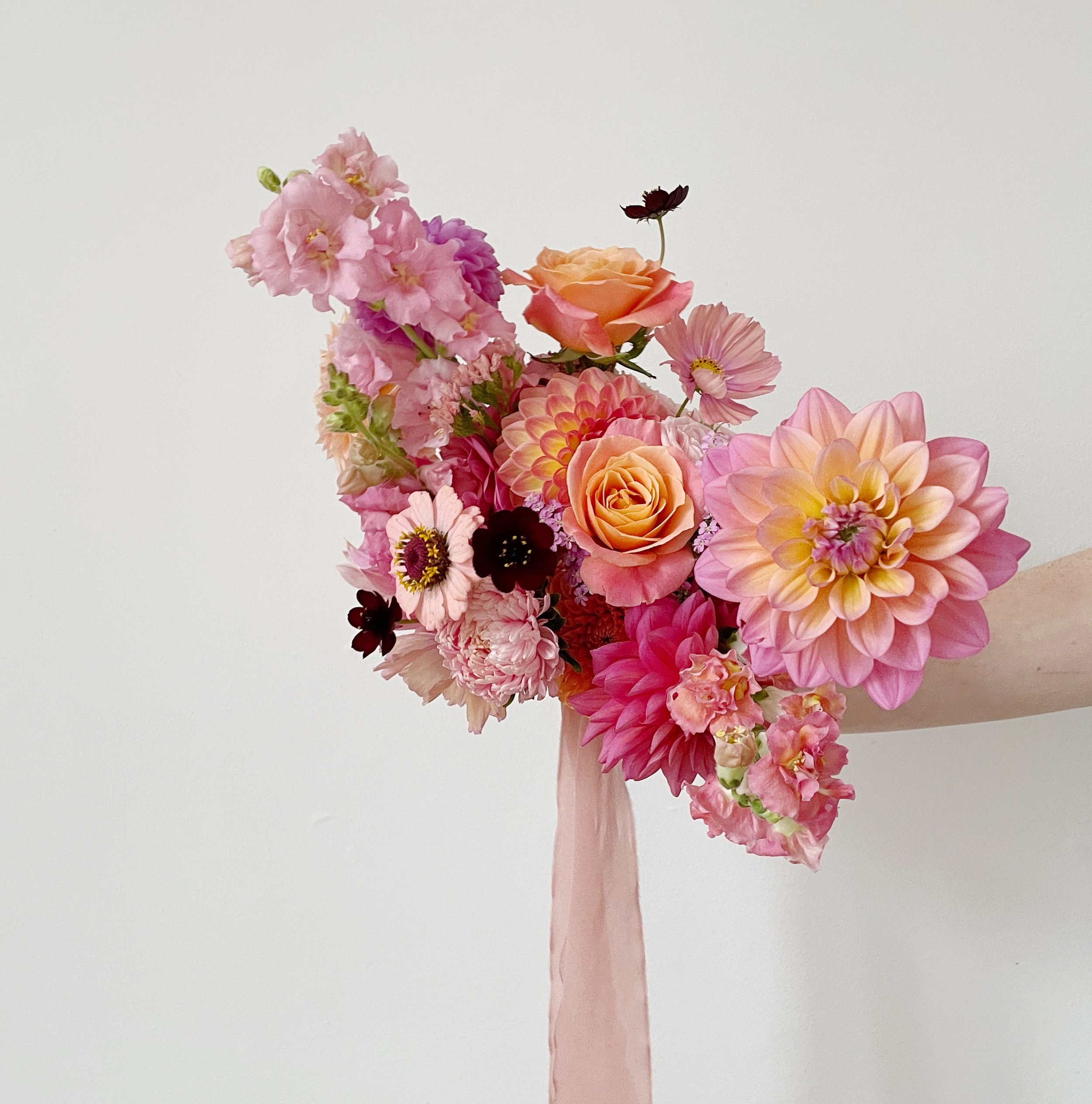 A colorful bouquet of pink, peach, and purple flowers in a pink vase against a white background.