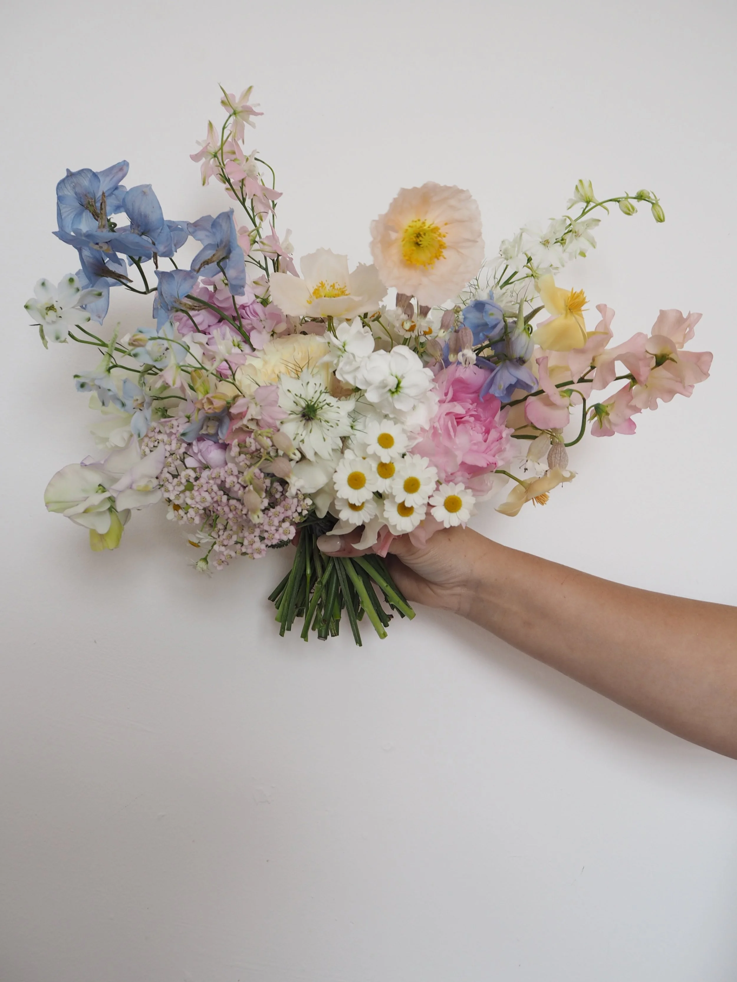A pretty and romantic bridal bouquet from July, full of British grown stems with delphinium, poppies, larkspur and daisies.