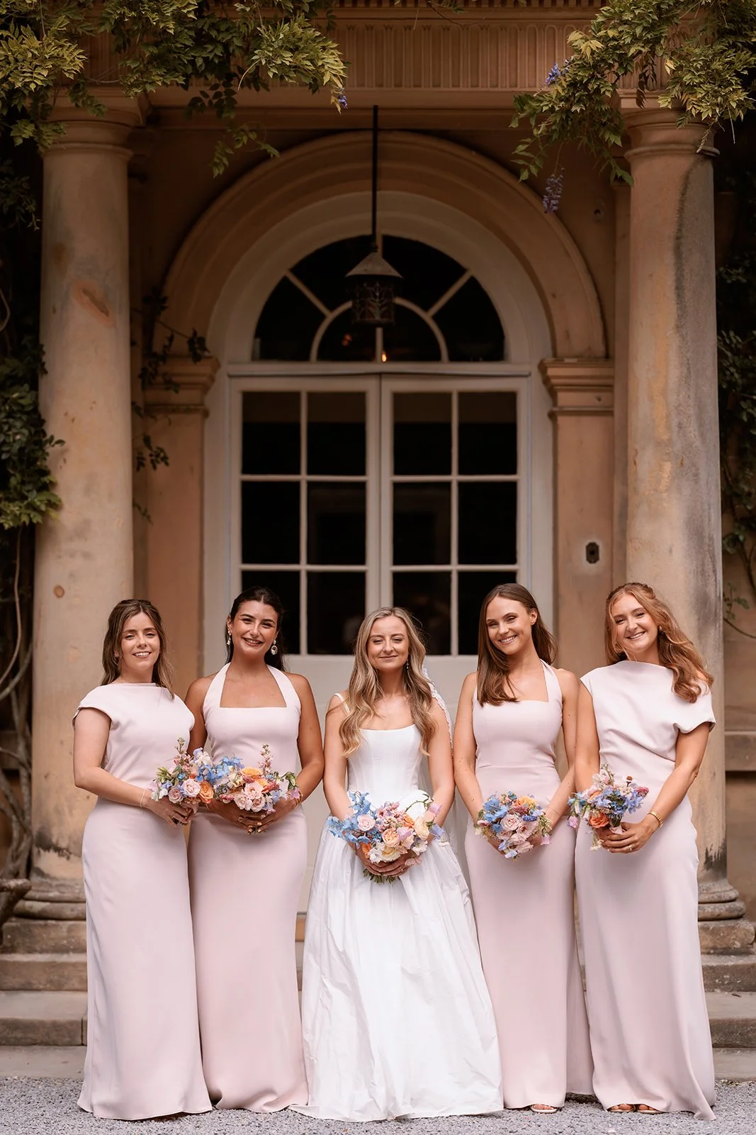 Bride and her bridesmaids wearing pastel pink and holding beautiful summer bouquets in pastel colours of butter yellow, pale pink, lilac, sky blue and coral, at Middleton Lodge, North Yorkshire