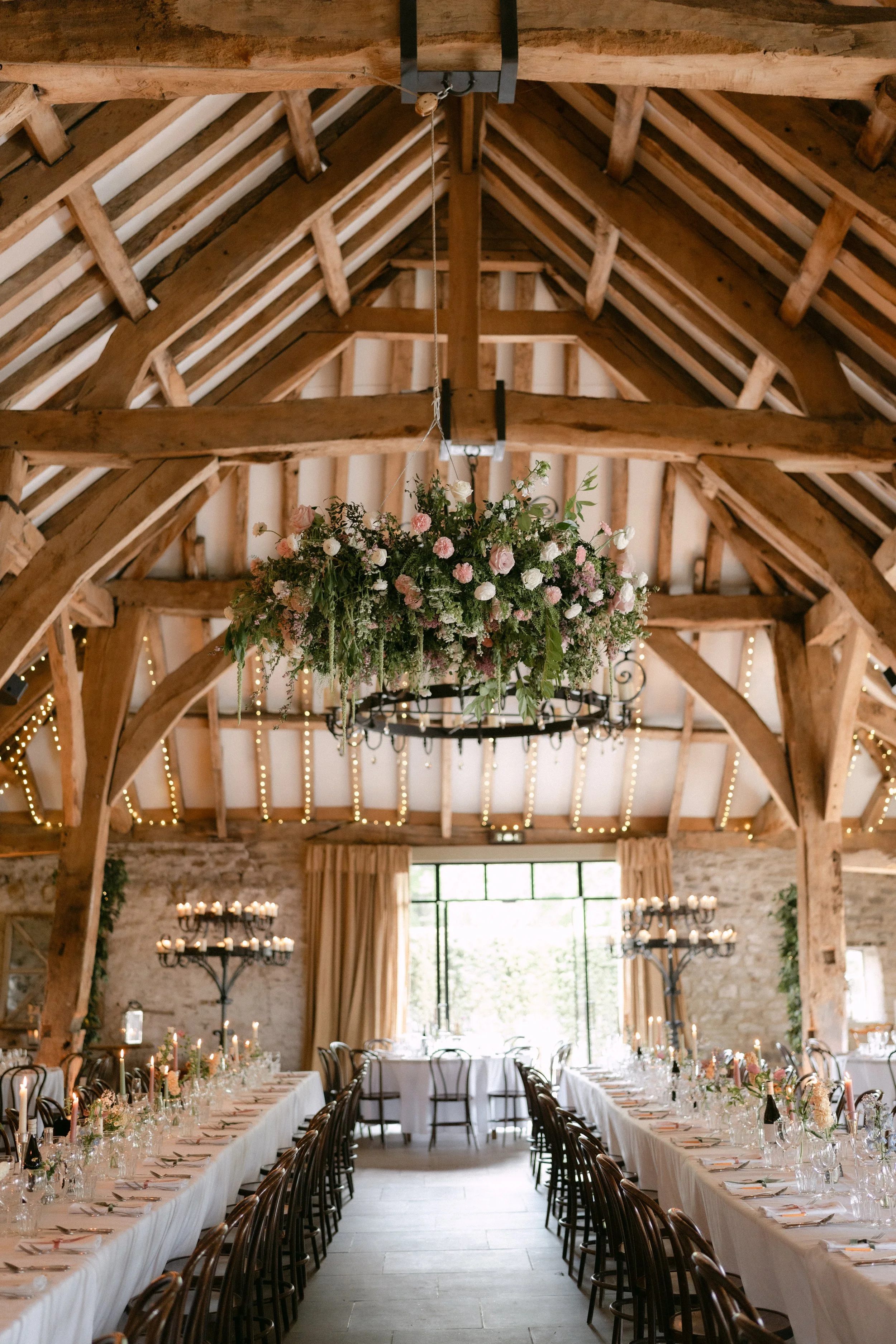 The Tithe Barn at Bolton Abbey with hanging hoop installation and trestle tables laid out ready for guests with white table cloths and bud vases 