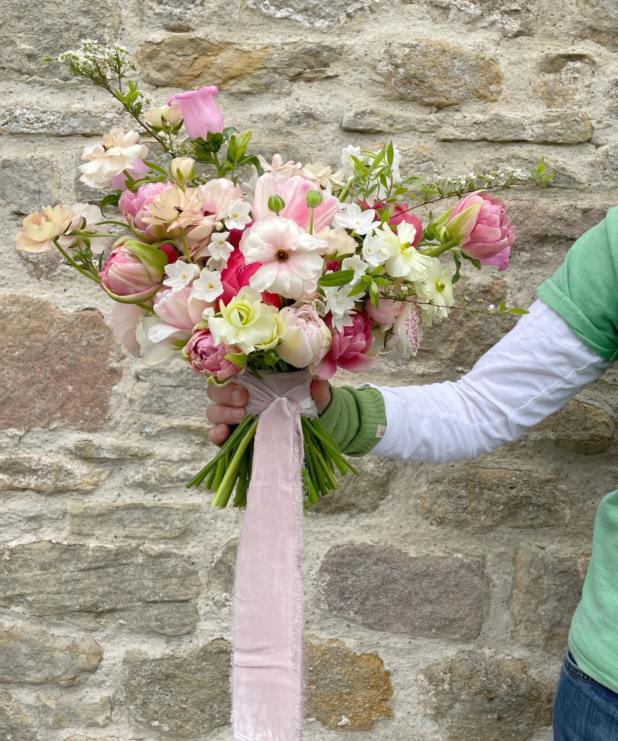 bridal bouquet in pinks, whites and greens, spring flowers butterfly ranunculus, tulips, paper whites, campanula and tied with a pale pink velvet ribbon