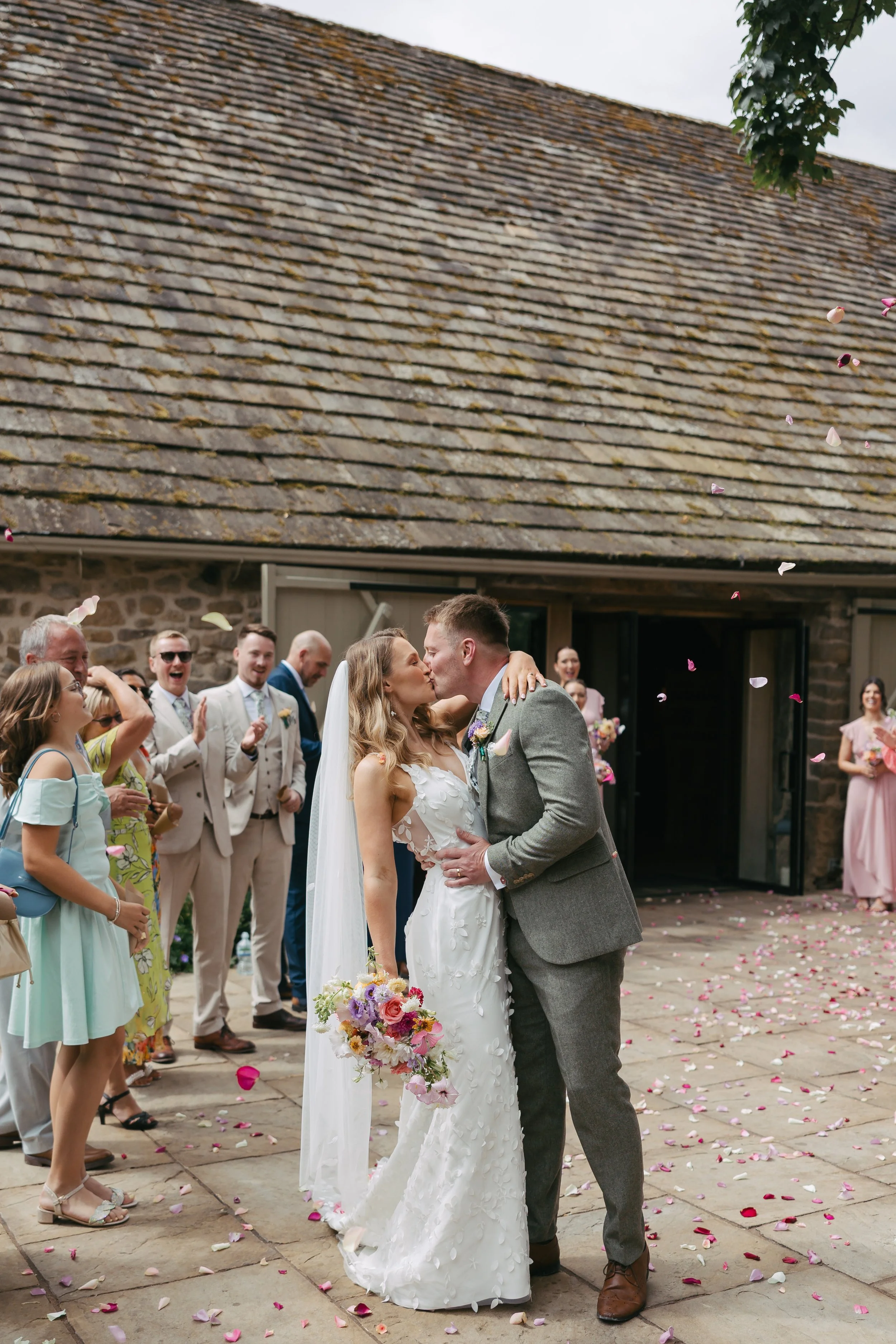 just married couple kissing with confetti in the air, modern bridal bouquet in pinks, whites, lilacs and corals, the Tithe Barn, Bolton Abbey, Yorkshire 
