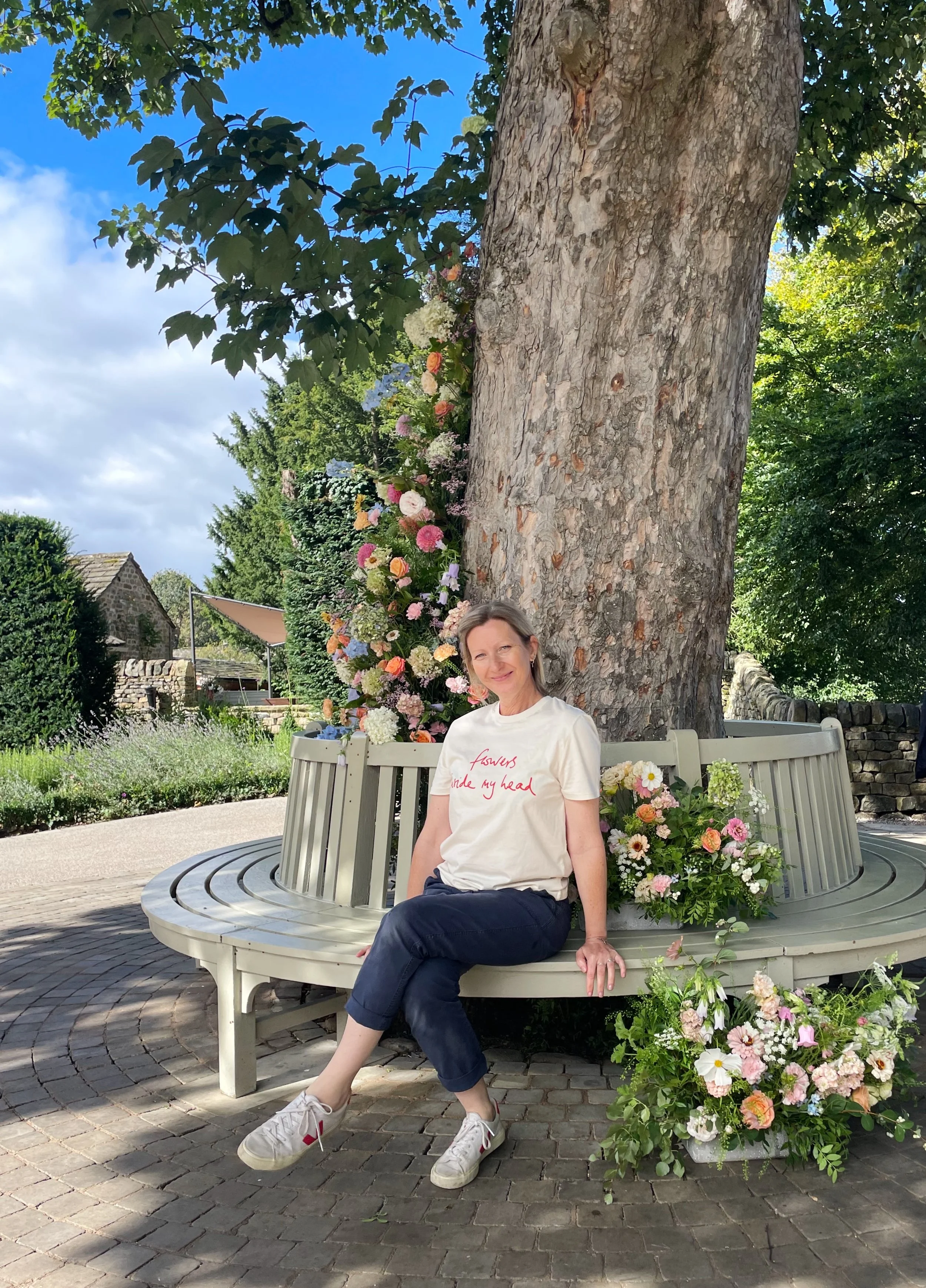 Bespoke floral artist, Sophie Warren-Smith from Flowers Inside My Head sitting down next to a tree wrapped with flowers at the Tithe Barn, Bolton Abby, North Yorkshire