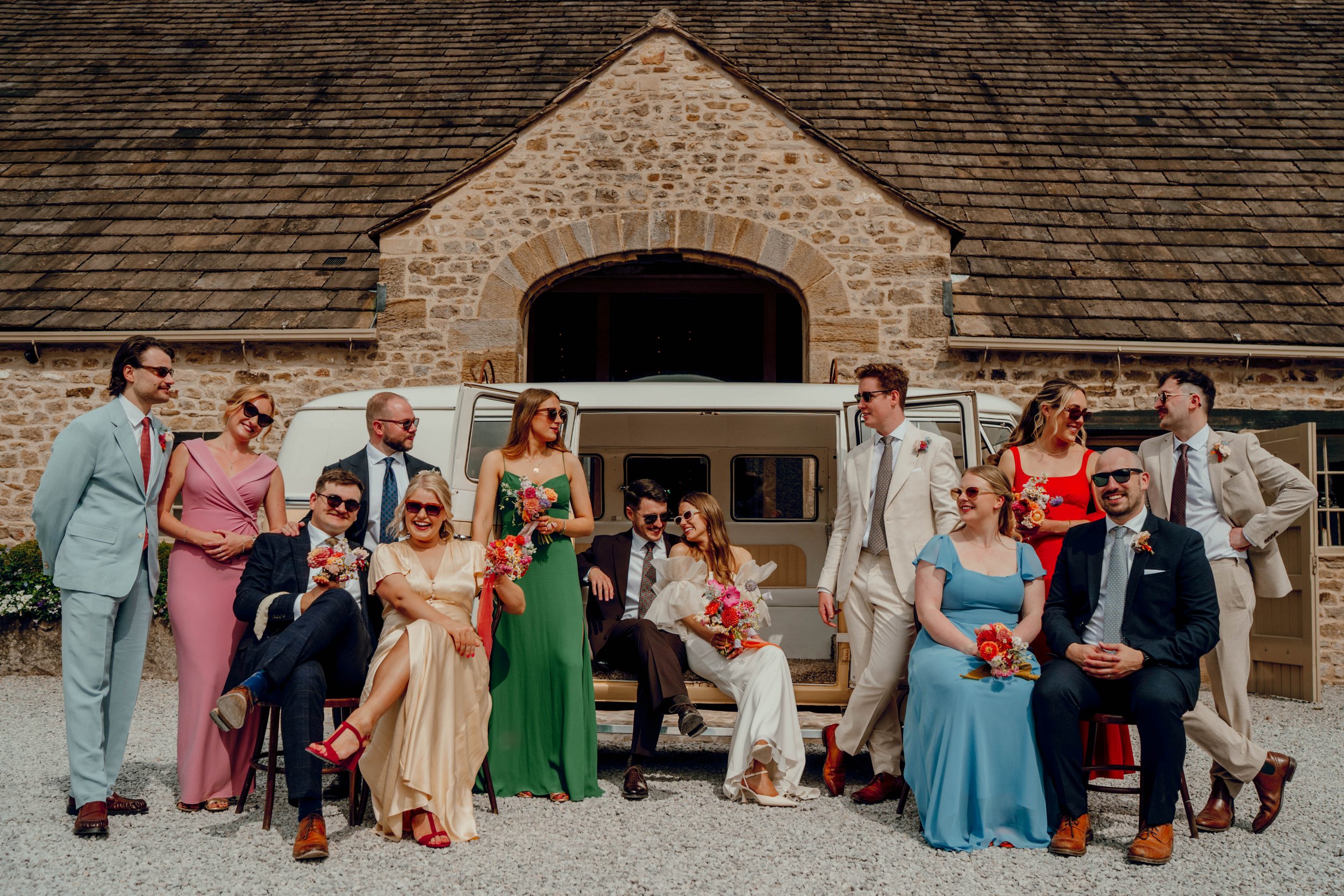 Image of married couple sat in a vintage VW van with bridesmaids and friends gathered around them outside the Tithe Barn, Bolton Abbey, Yorkshire