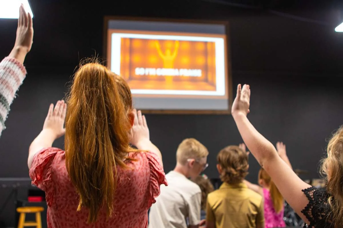 Kids raising their hands in sync with a video playing on the screen.