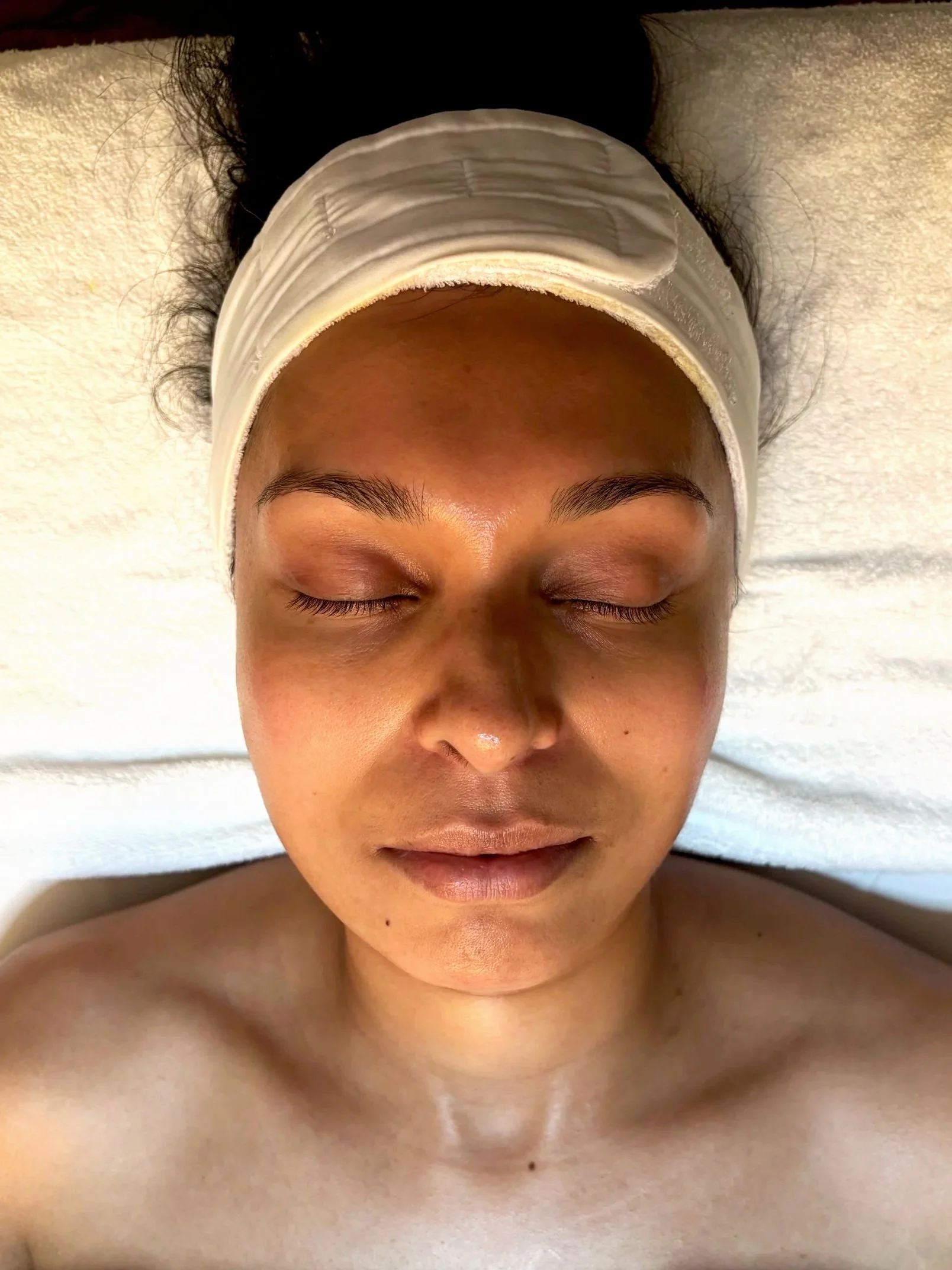 A woman with closed eyes, lying on her back, wearing a white headband, with a neutral facial expression.