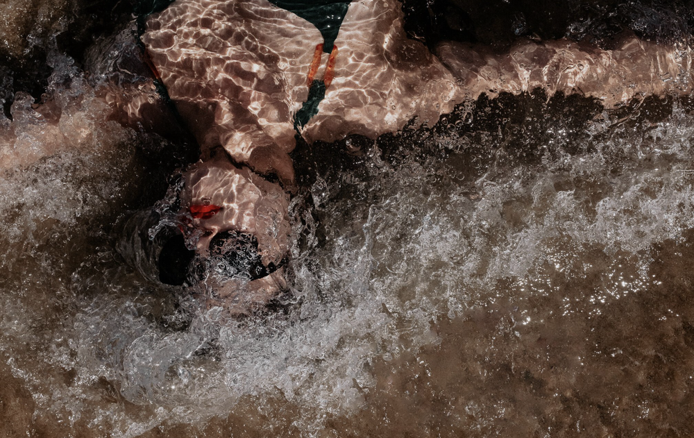 Waves Within: a swimmer with red goggles surrendering to churning water
