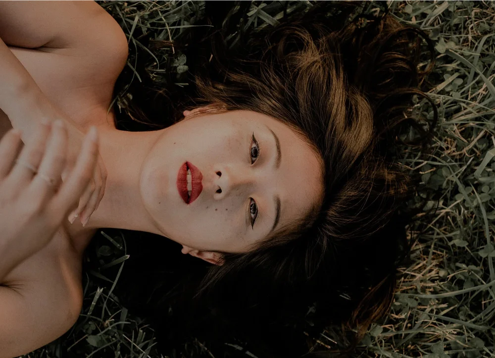 Portrait of a woman with red lipstick lying in the grass