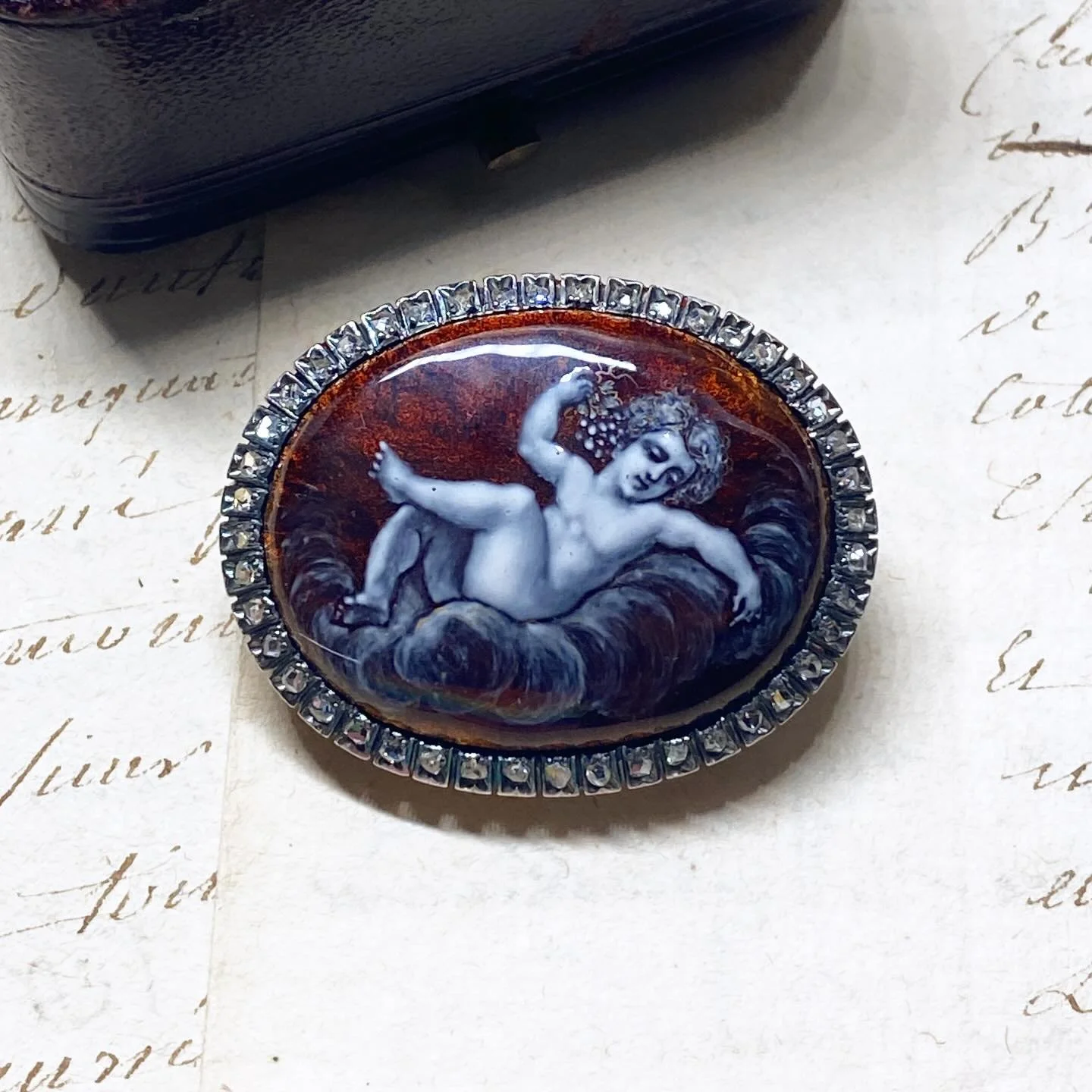 A lovely antique brooch from the second half of the 19th century, crafted in 18 karat rose gold and silver, set with rose-cut diamonds and Limoges enamel, depicting a cherub playing with grapes.
 
This figure is a classic artistic theme of inspired t