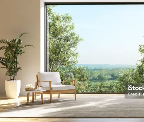A cozy indoor seating area near a large window showcasing a lush green landscape with trees and a clear blue sky.