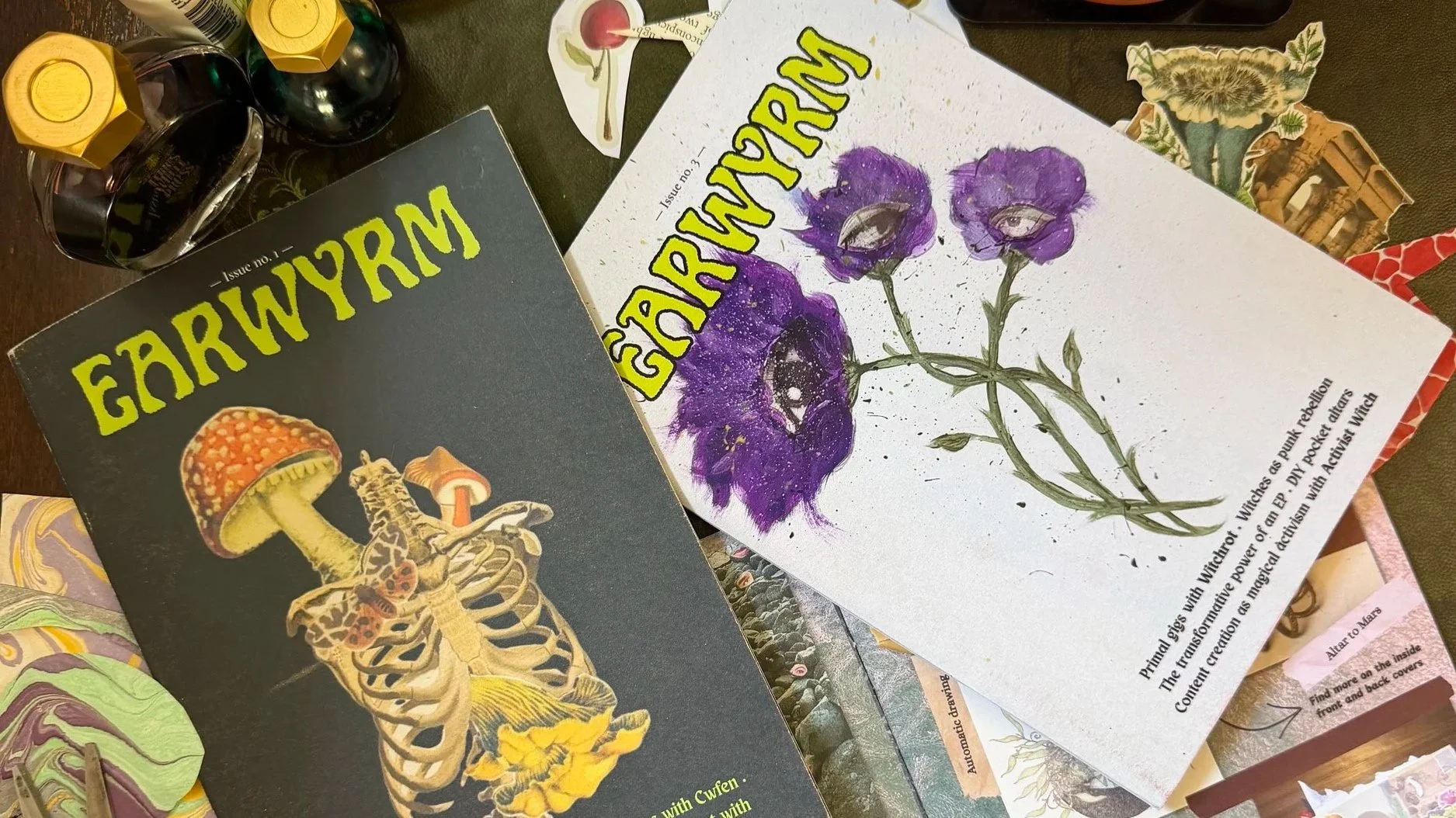 top down shot of three copies of earwyrm spread out on a green leather topped desk, with some paper clippings scattered beneath them.