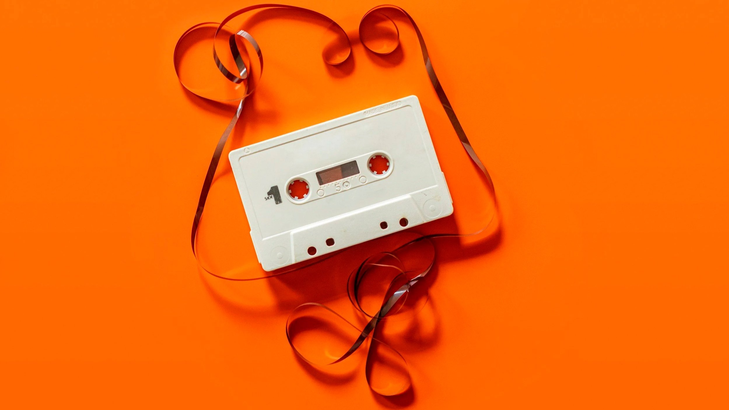 bright orange background with a plain white unspooled cassette tape on it.