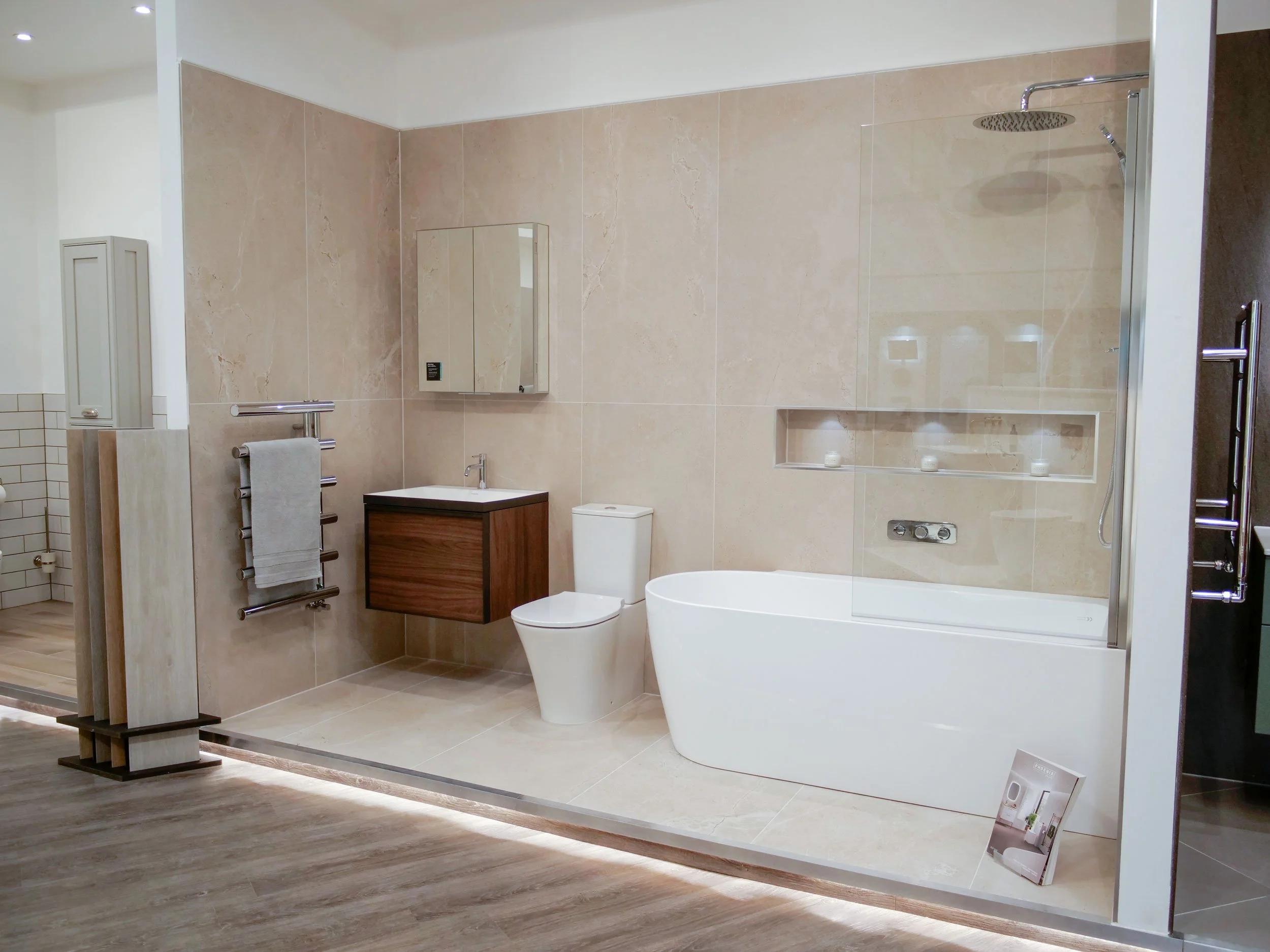 Modern bathroom with a stand-alone bathtub, a toilet, a small vanity with a mirror, and a towel rack, all in neutral tones with tiled walls and wooden flooring.
