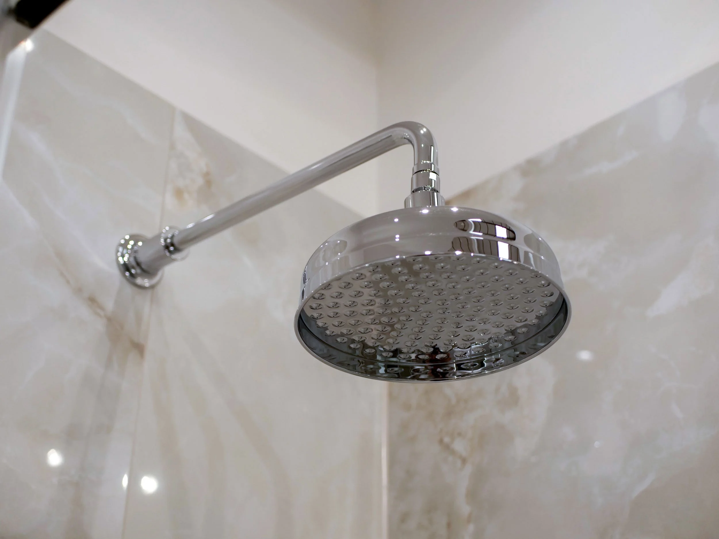 Chrome showerhead attached to a shower arm in a tiled bathroom.