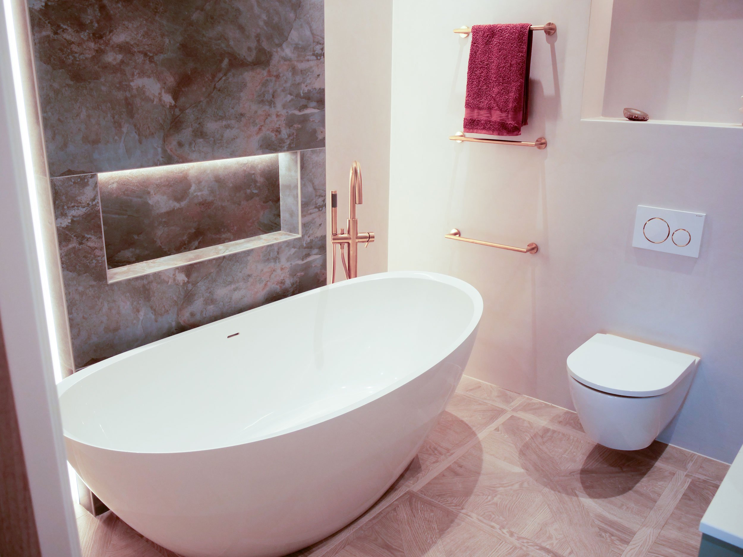 Modern bathroom with a freestanding bathtub, dark marble wall, and a wall-mounted toilet.