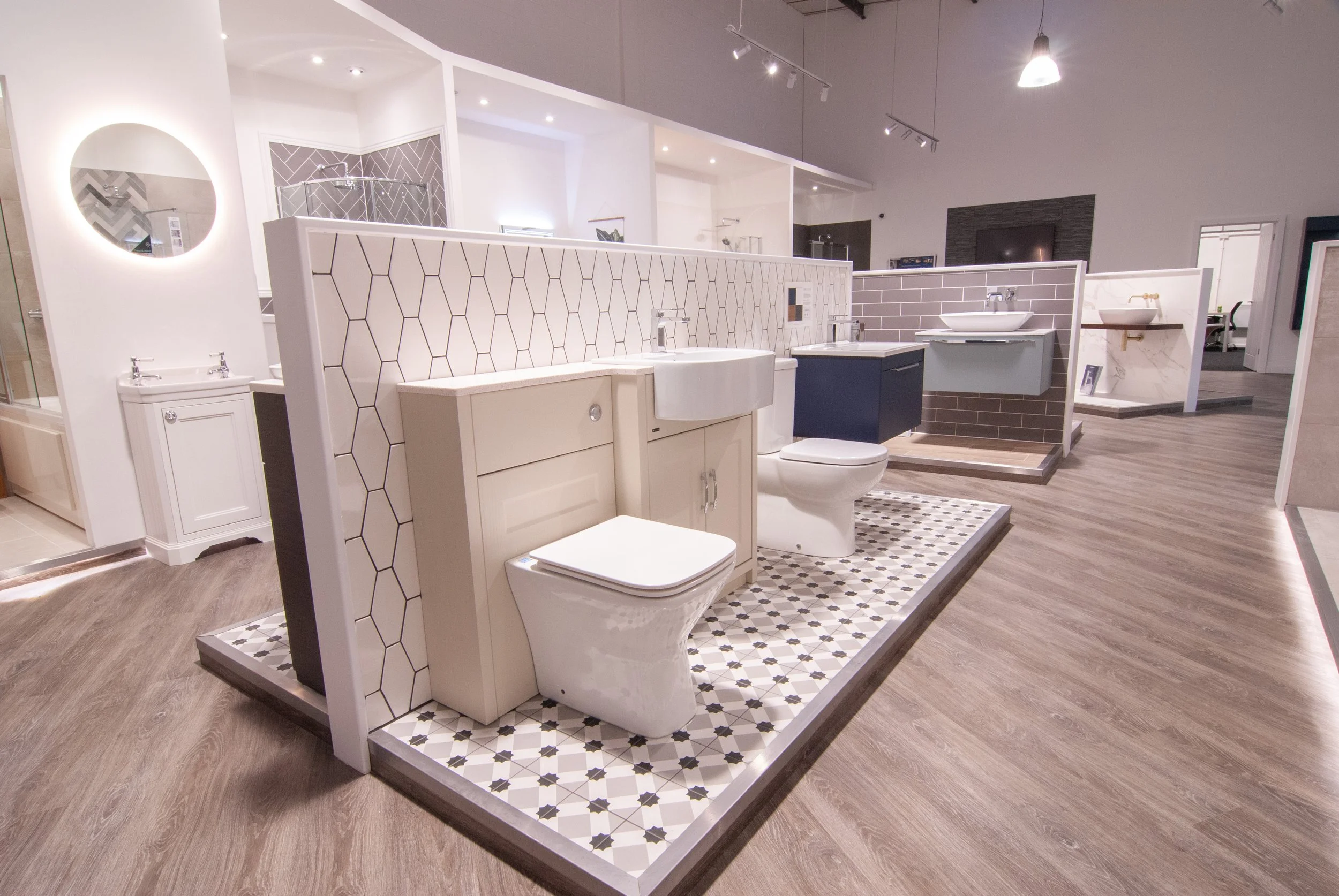 Display of bathroom fixtures on a showroom floor, including toilets, sinks, and vanities with various tile and wall designs.