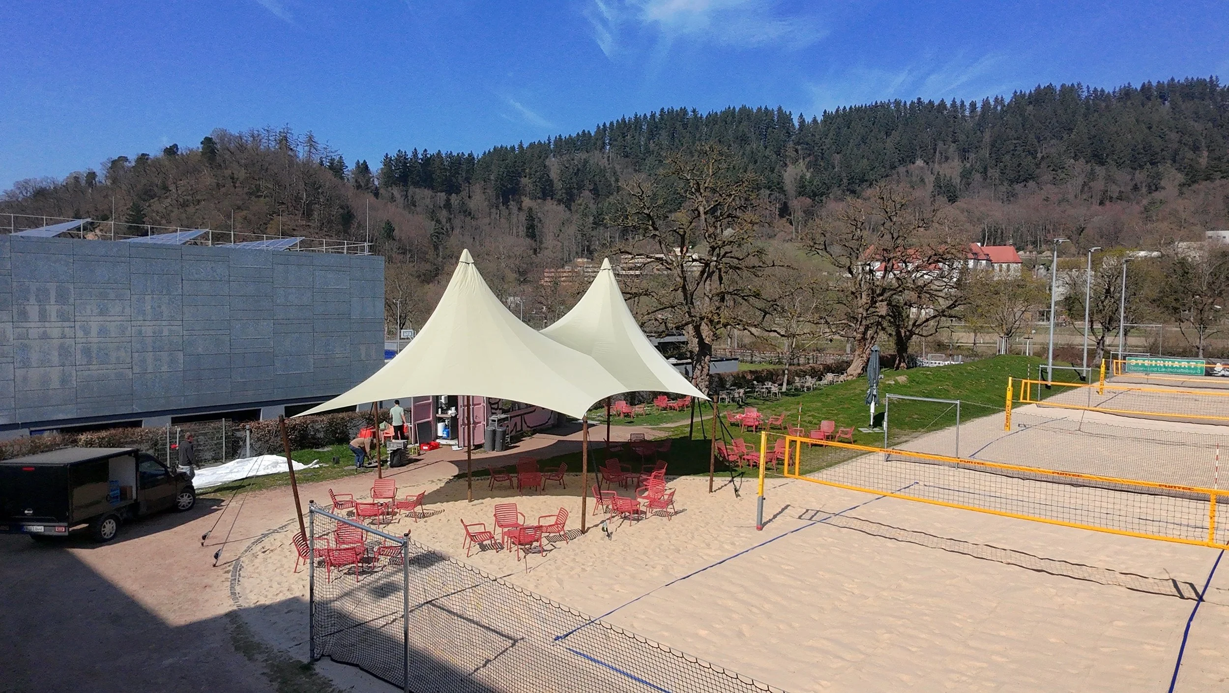 Umfassende Luftaufnahme des HOKK in Freiburg mit dem großen Phoenix-Sonnensegel Gastronomie von Tentsetter über dem Kiosk und Beach-Volleyball-Bereich.