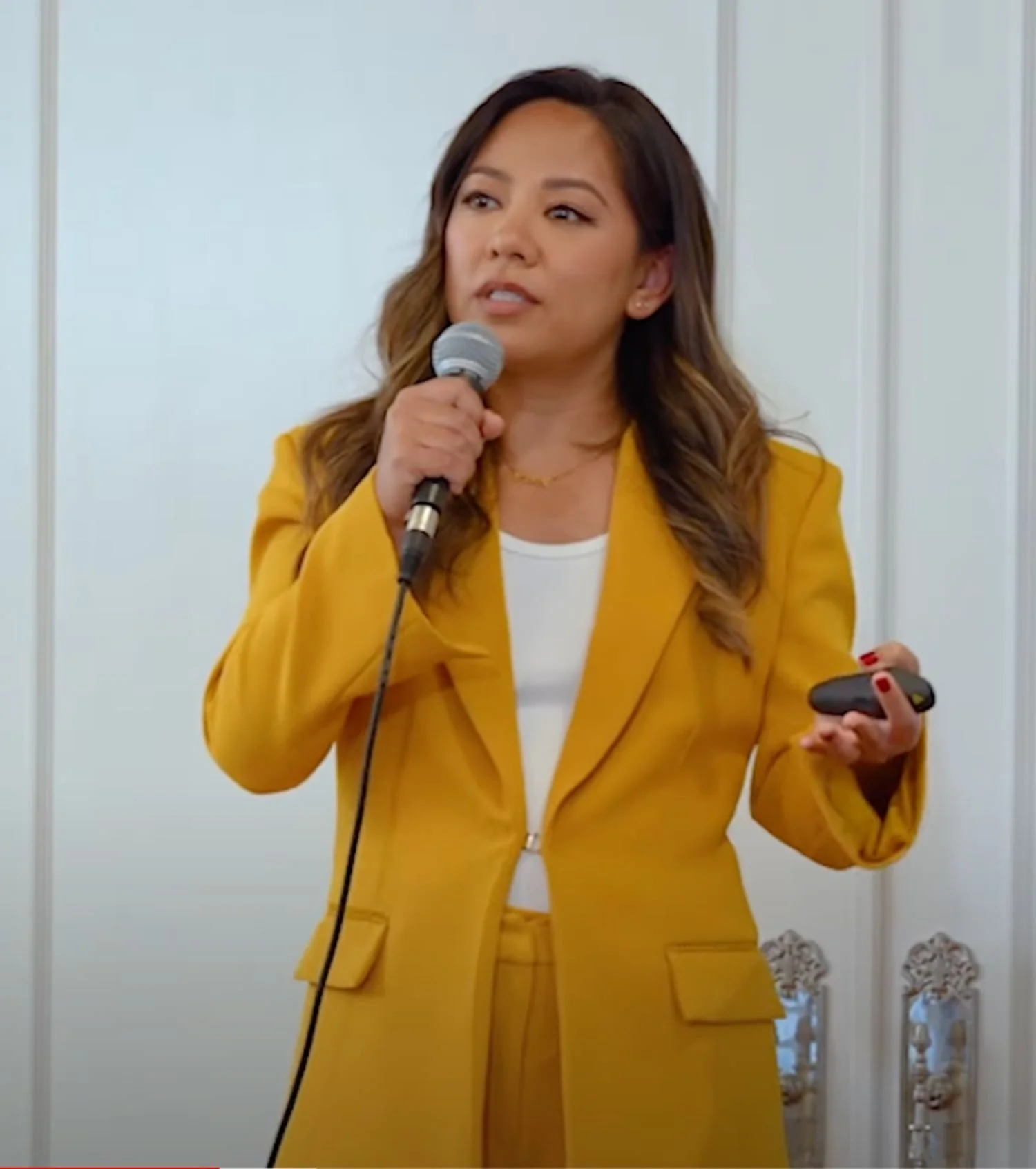 Woman in a yellow blazer speaking into a microphone during a presentation.