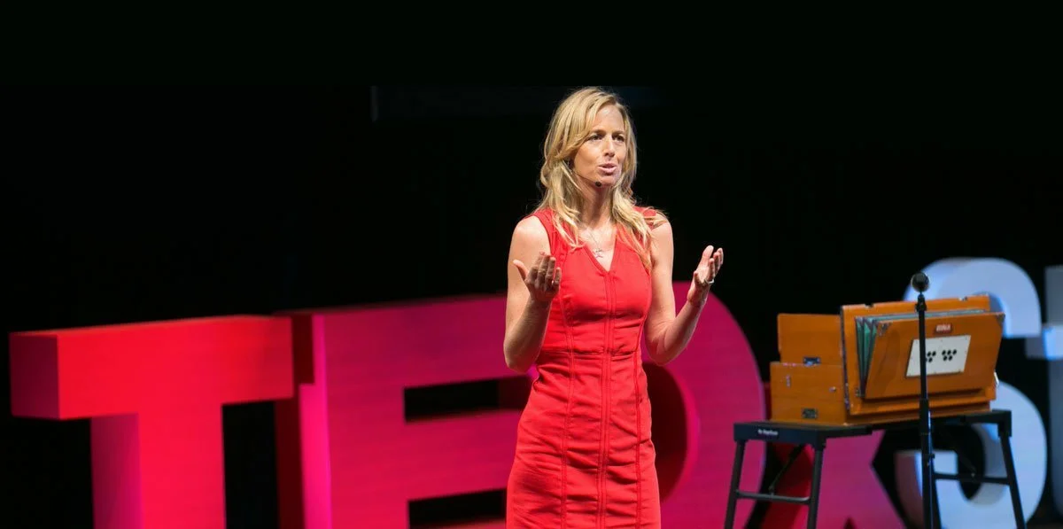 A woman in a red dress giving a speech on stage at a TED event.