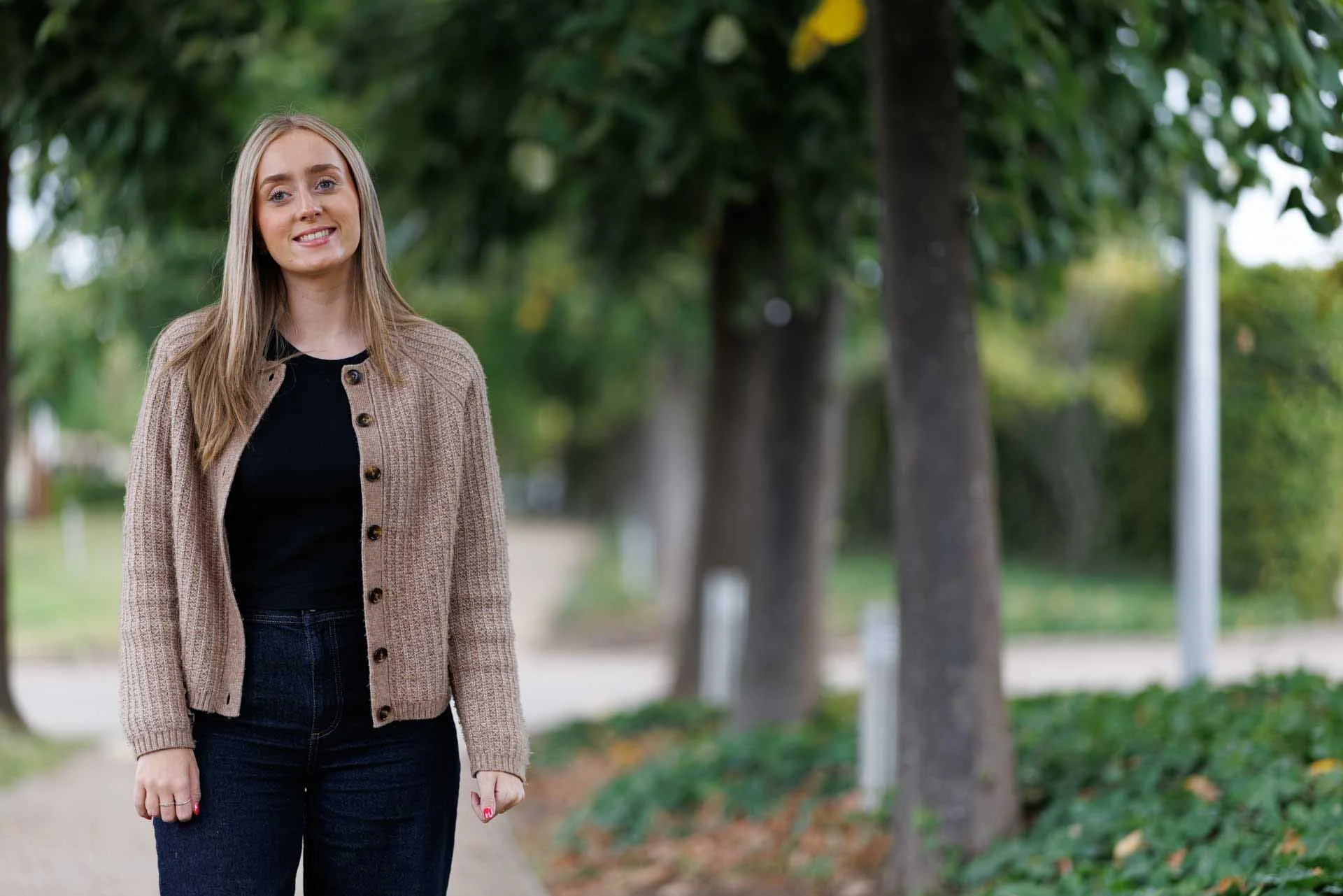 A woman with long blond hair standing near some trees
