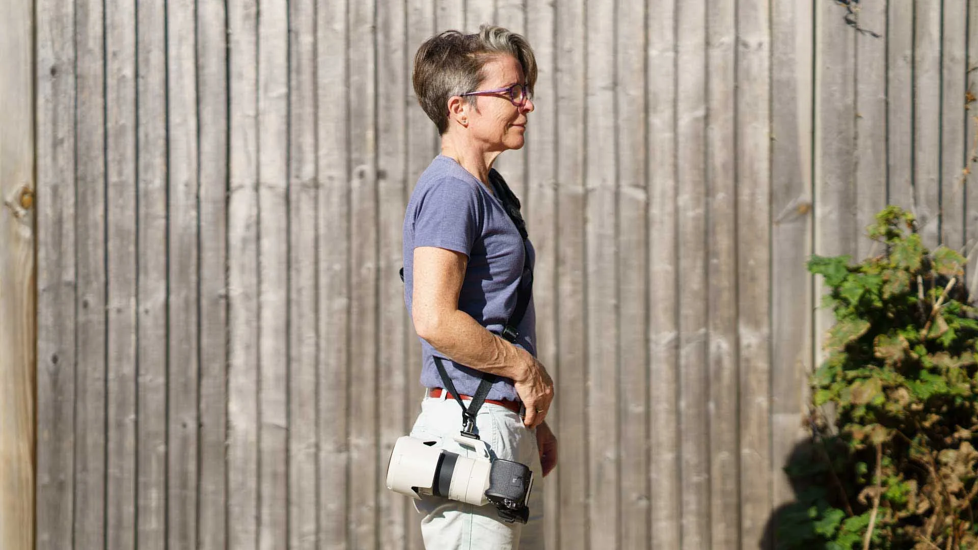A side view of Angela Nicholson while she carries a camera with a telephoto lens on the 3 Legged Thing Axis Sling