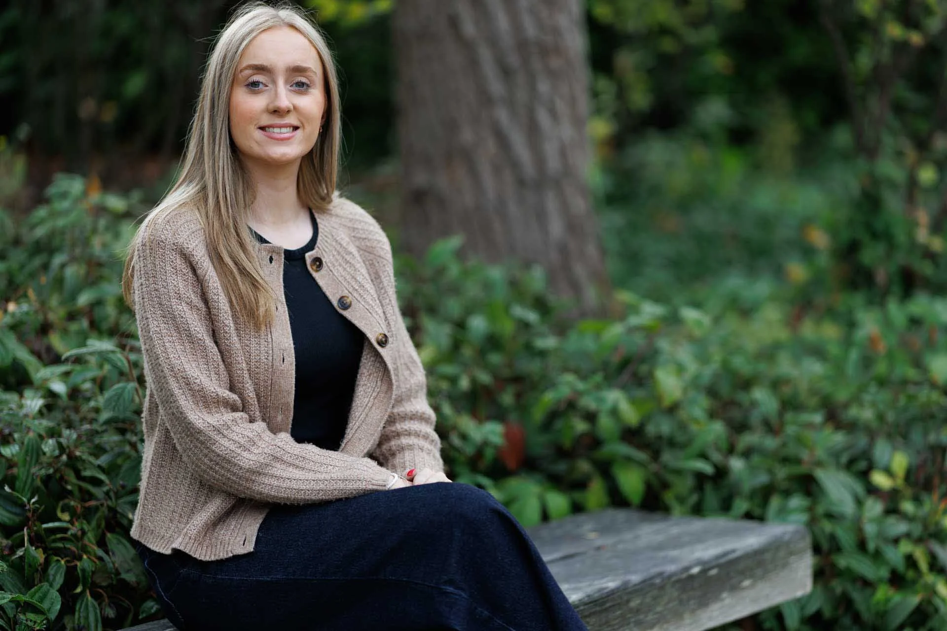 A woman with blond hair sat on a bench near some bushes