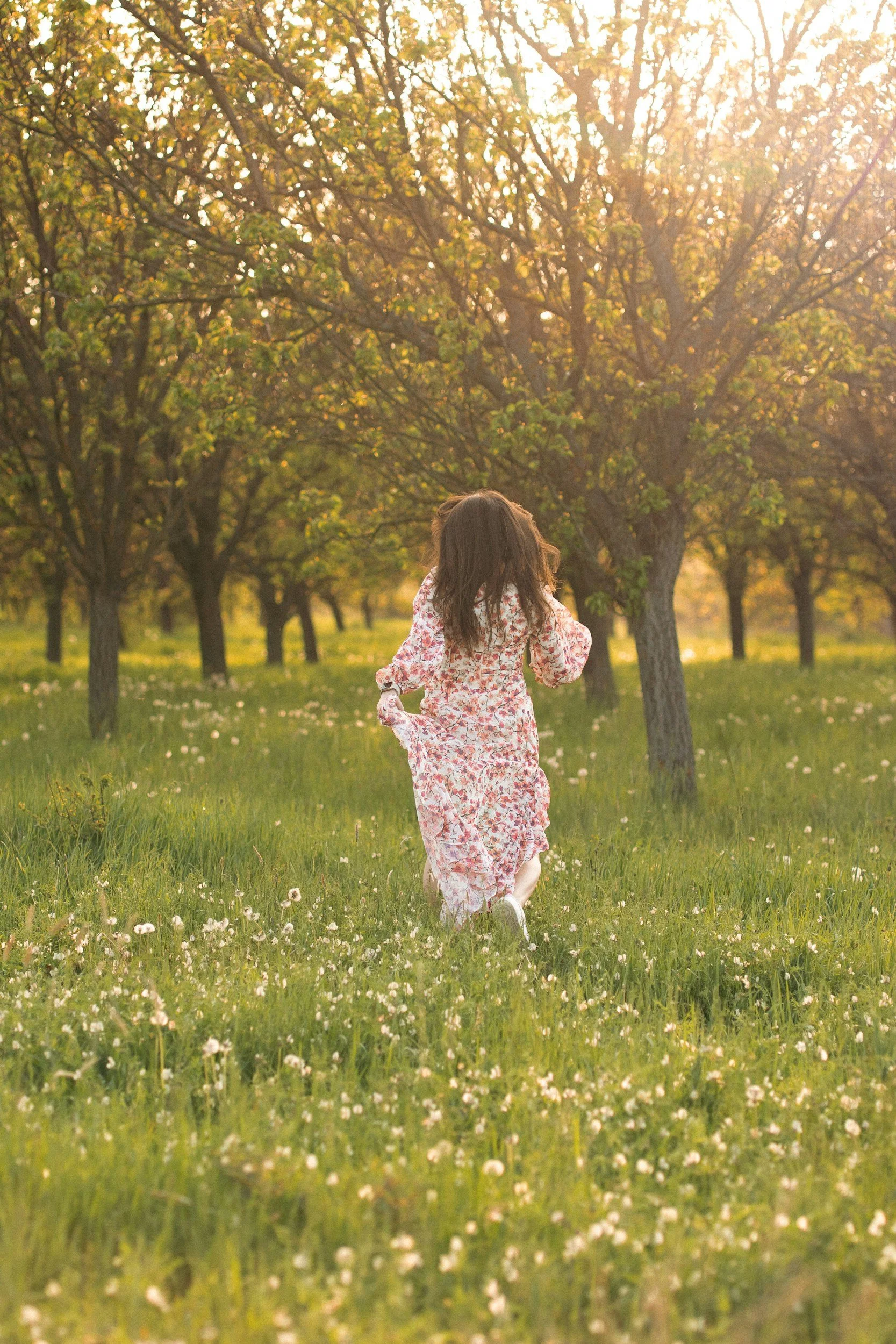 Woman in a floral dress running through afield of flowers toward trees due to reduced trauma from AEDP therapy in Colorado
