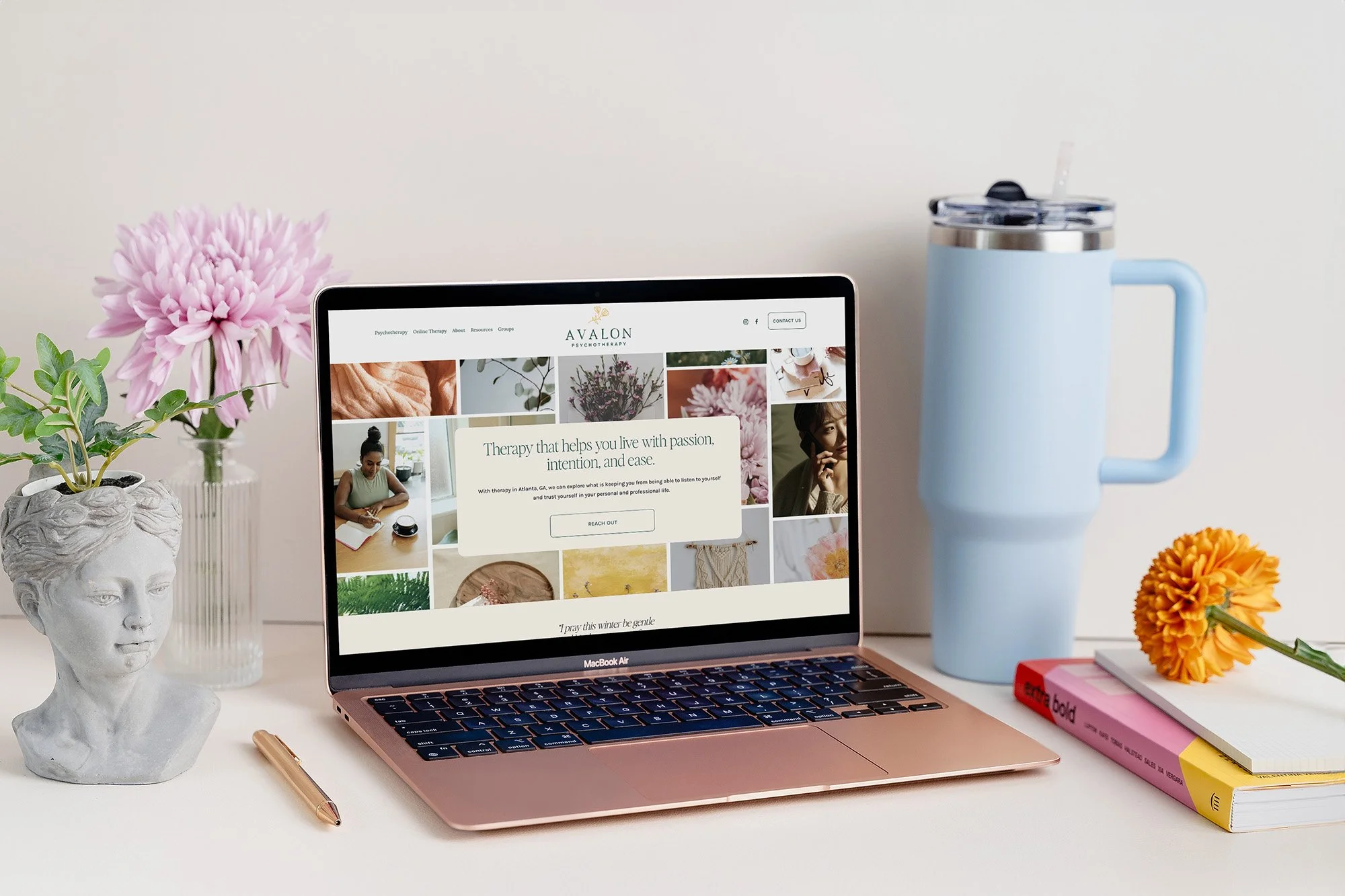 Computer with vase of flowers, books, and water tumbler