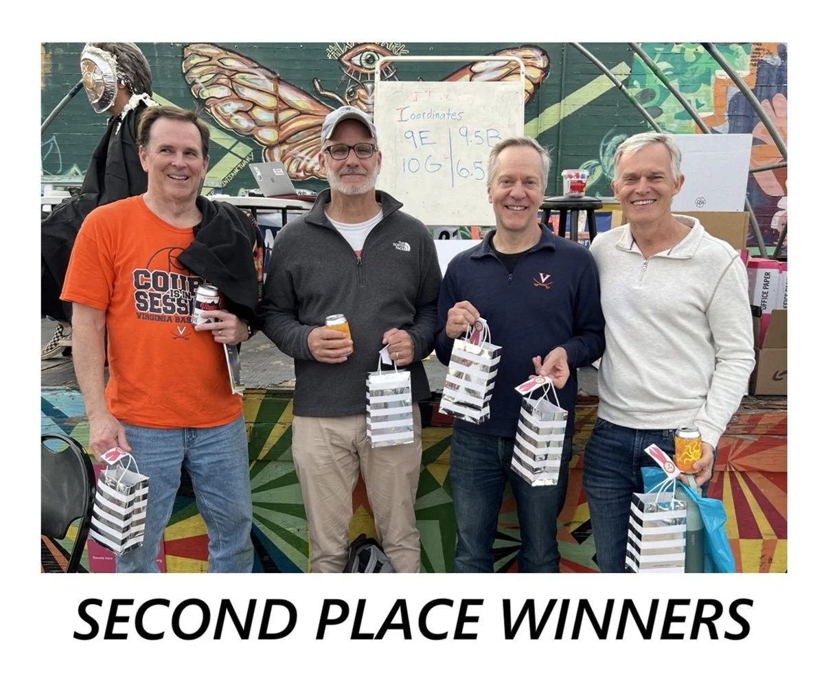 A group of four people, the second place winners, stand for a picture, each holding a silver and white gift bag.
