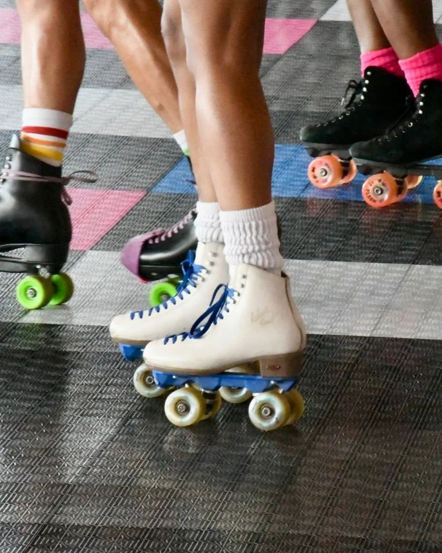 Close-up of people wearing ice skates on a skating rink, with colorful tiles on the floor and some wearing bright socks.