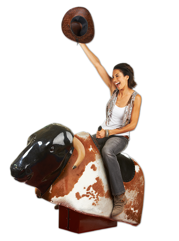 A woman riding an arcade-style mechanical bull, holding a cowboy hat in the air, smiling and wearing casual clothes against a black background.