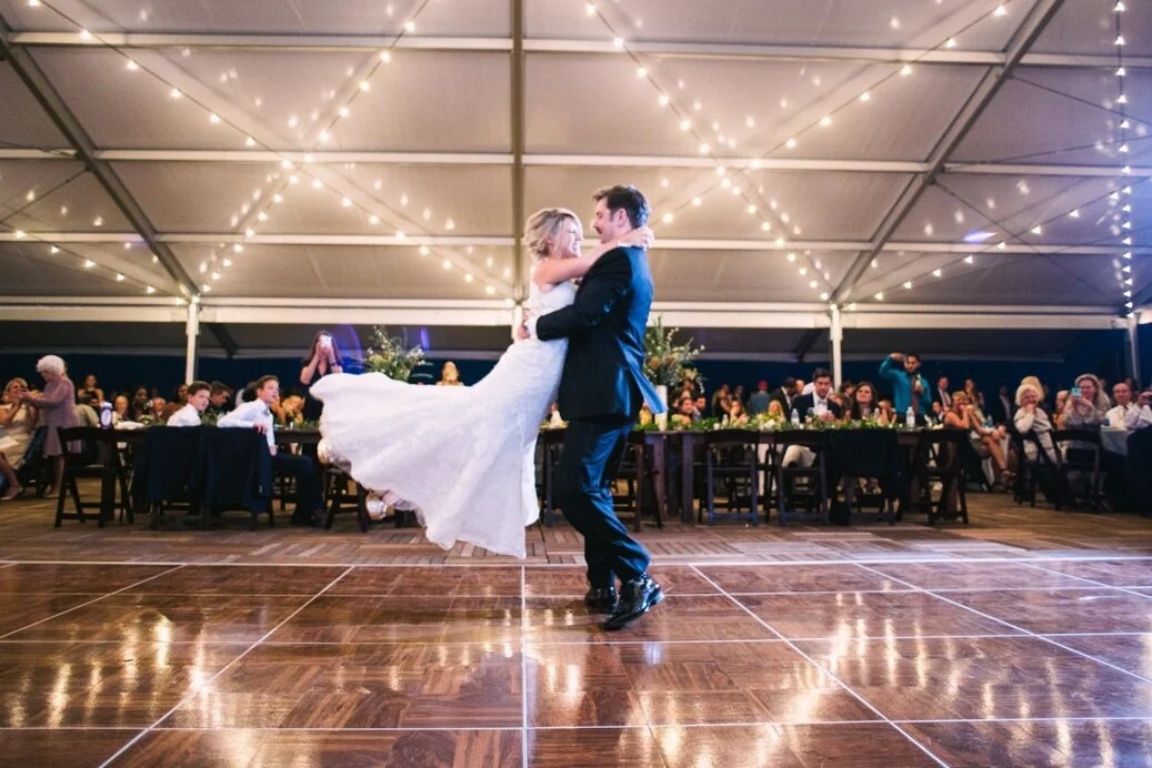 A bride and groom dancing at their wedding reception under string lights in a decorated tent.
