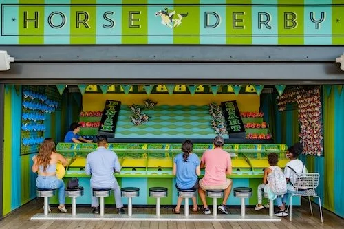 People playing the horse derby carnival game at an amusement arcade.