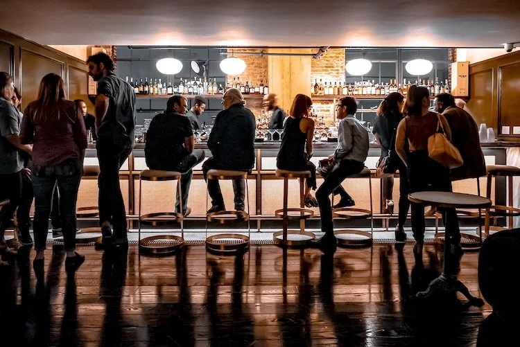 People sitting and standing at a bar in a restaurant or pub with warm ambient lighting.