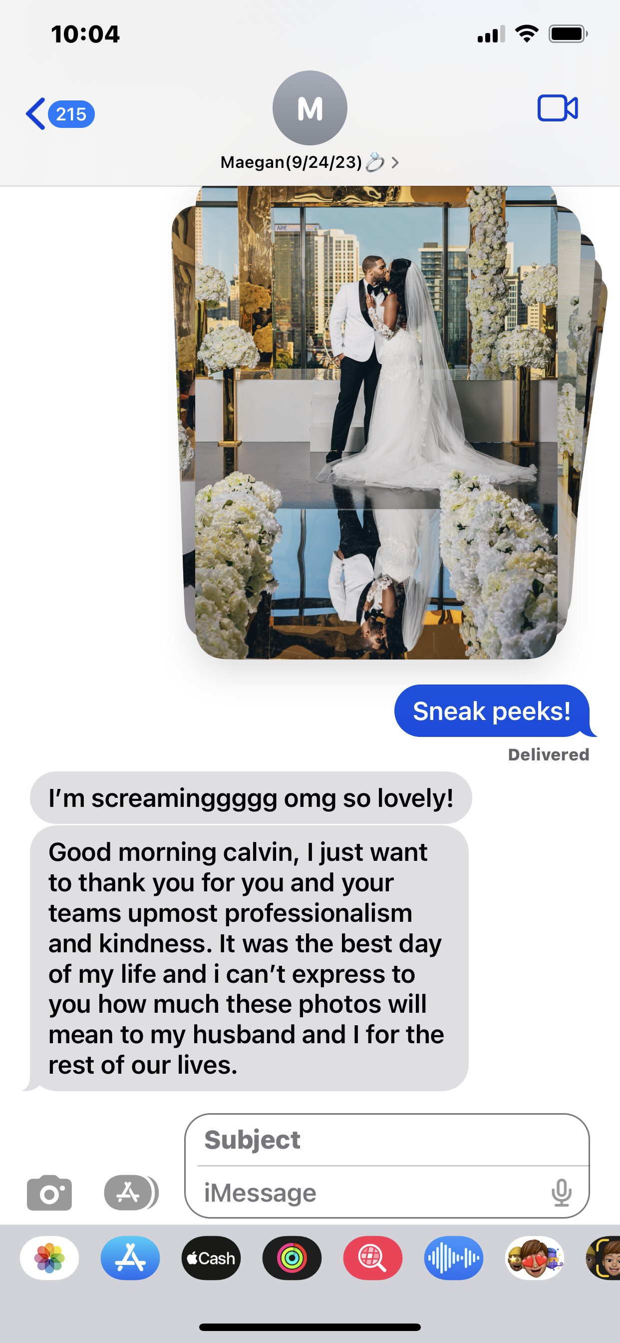 A wedding photo of a bride and groom sharing a kiss on a decorated stage with city buildings in the background. The stage is adorned with white and yellow flowers and gold accents, with a reflective floor.