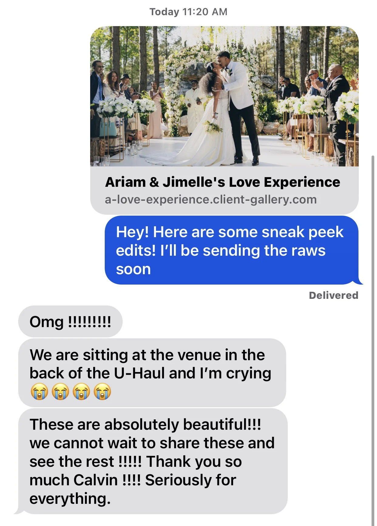 A wedding ceremony outdoors with a bride and groom kissing under a floral arch, guests seated on either side of the aisle, surrounded by trees and natural scenery.