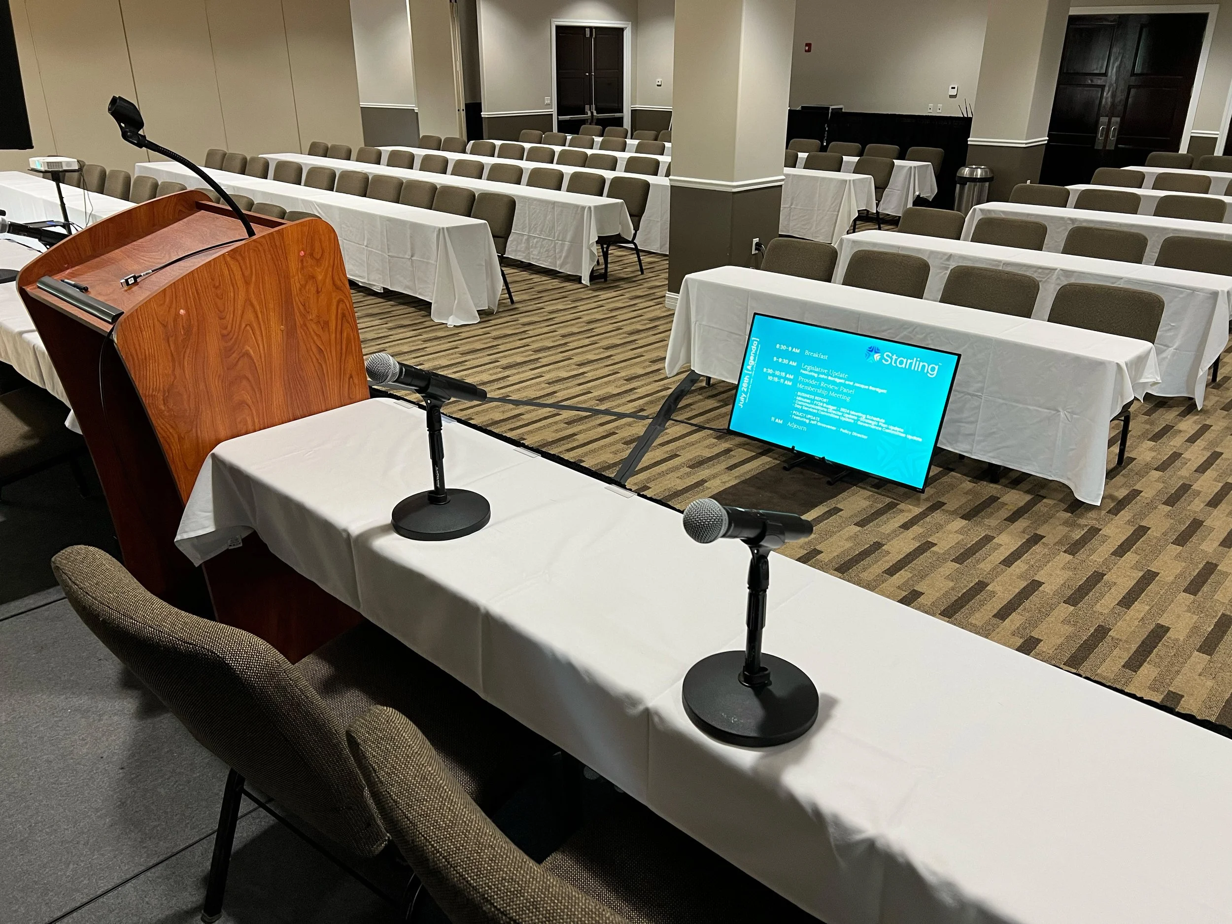 View from behind a presenter panel table looking at wireless microphones and confidence monitor in a classroom style breakout room in Missouri