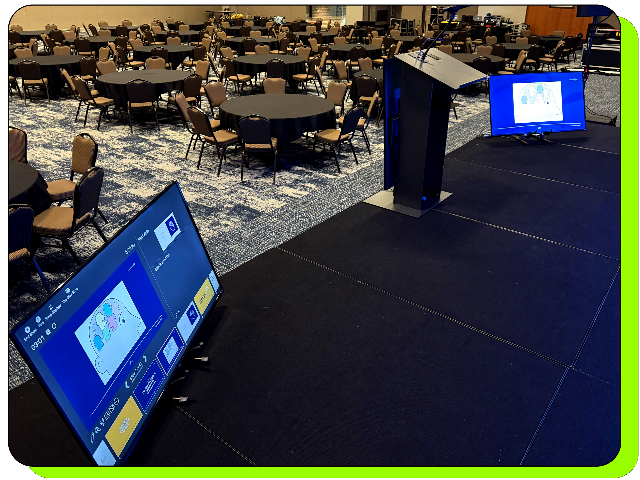 Two confidence monitors placed on a stage on either side of a podium which is centered. One monitor is displaying presenter notes, while the other monitor is displaying full screen slides at a conference in Missouri