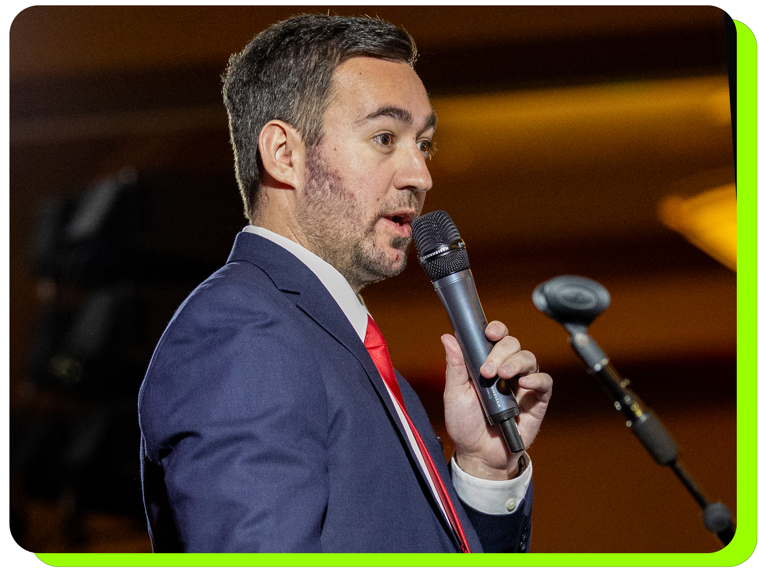 Man on stage speaking into a black handheld microphone using good mic technique