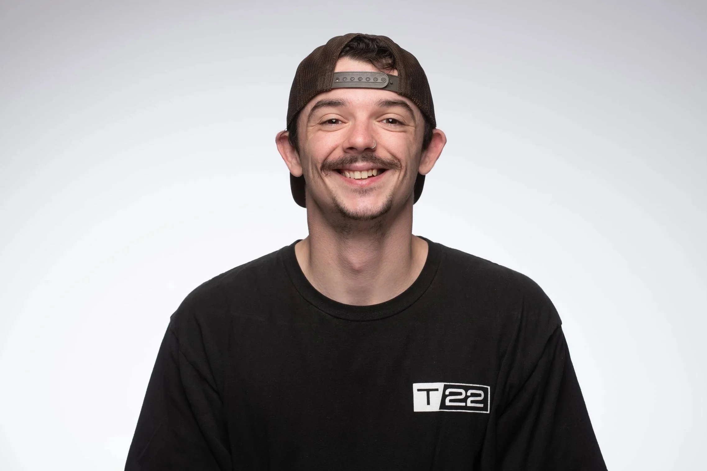 Young man with a baseball cap on backwards smiling at camera who is a video technician