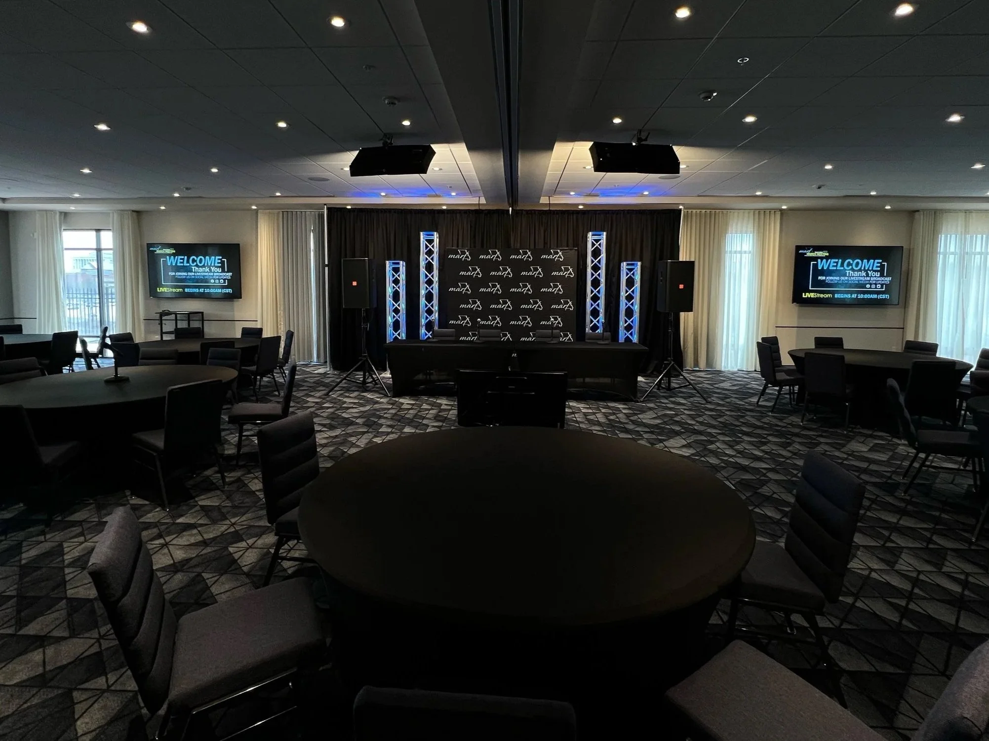 View from the audience looking at a panel table setup with lighting for a livestream, black pipe and drape, and audio setup in Missouri