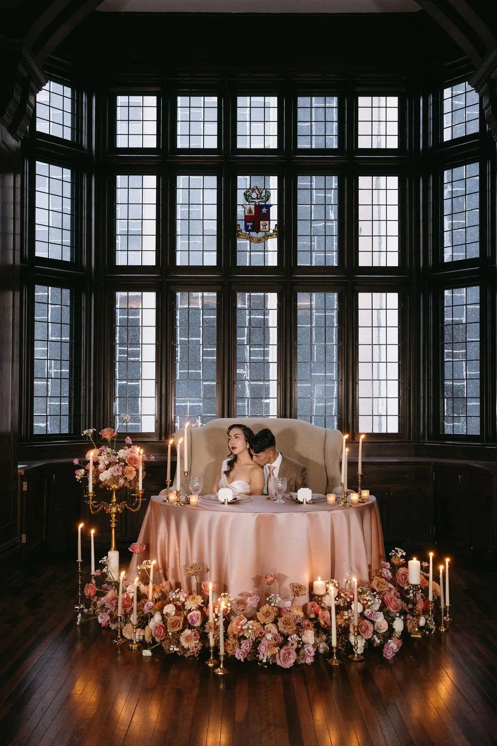 Vintage sweetheart table setup in front of a grid window surrounded by floor candles and lush moody floral arrangements.