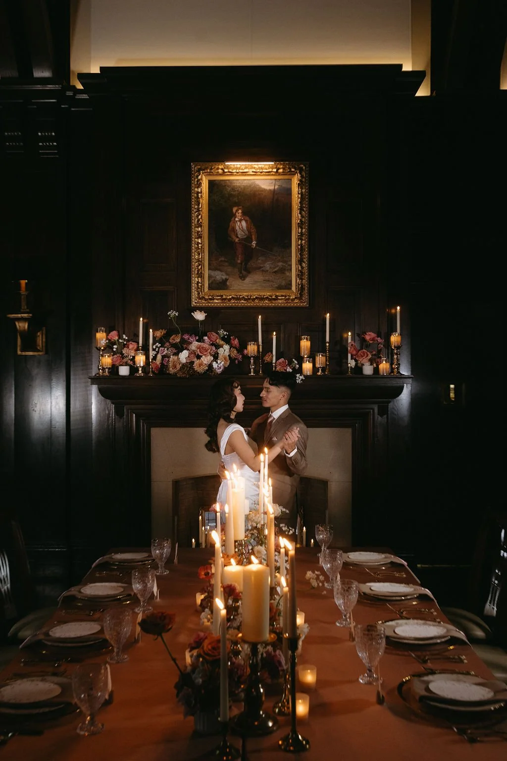 Moody candlelit wedding reception table with gold candelabras, dark wood finishes, and elegant vintage venue lighting.