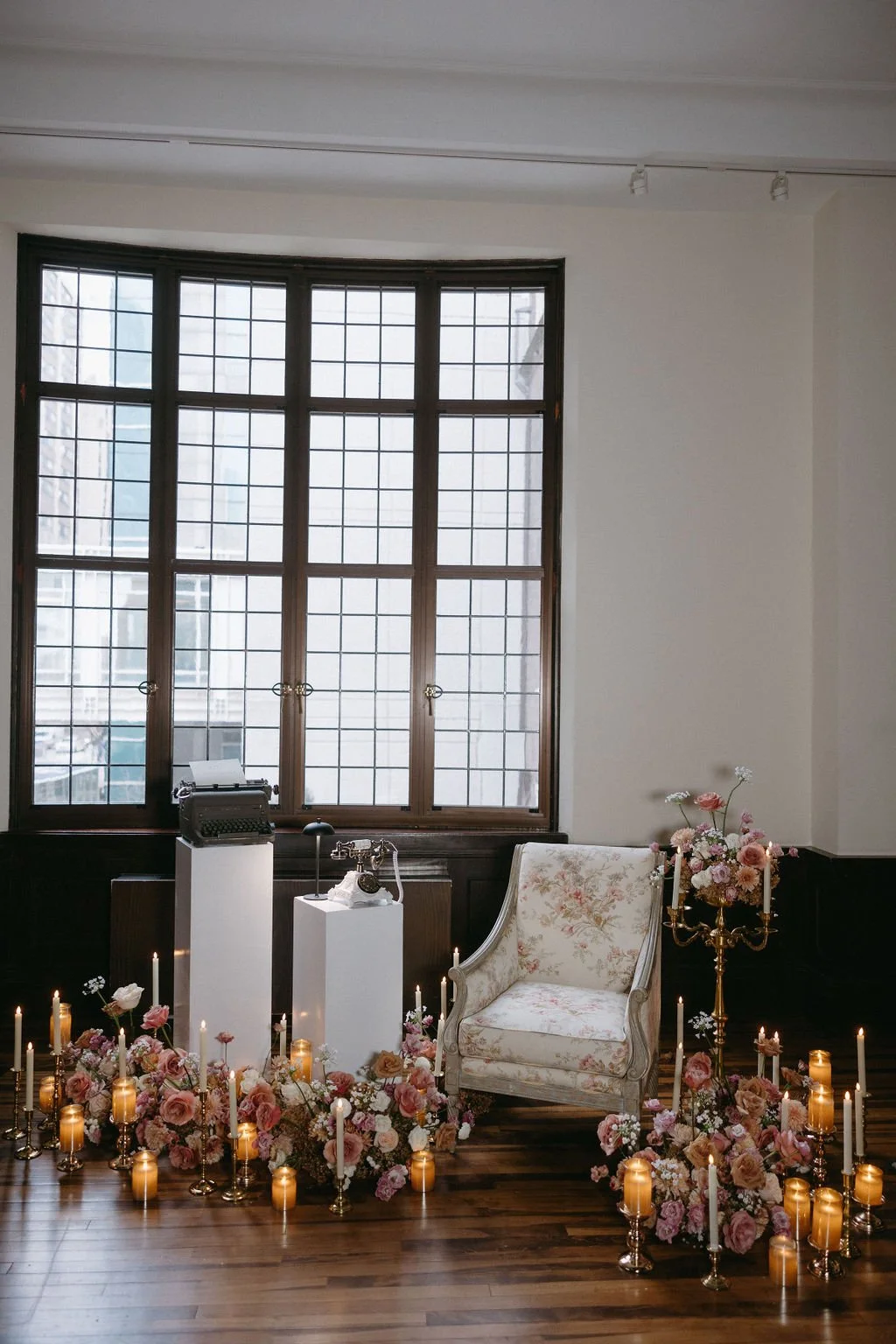 Tall industrial window backdrop featuring vintage brass candlesticks and glowing white taper candles.