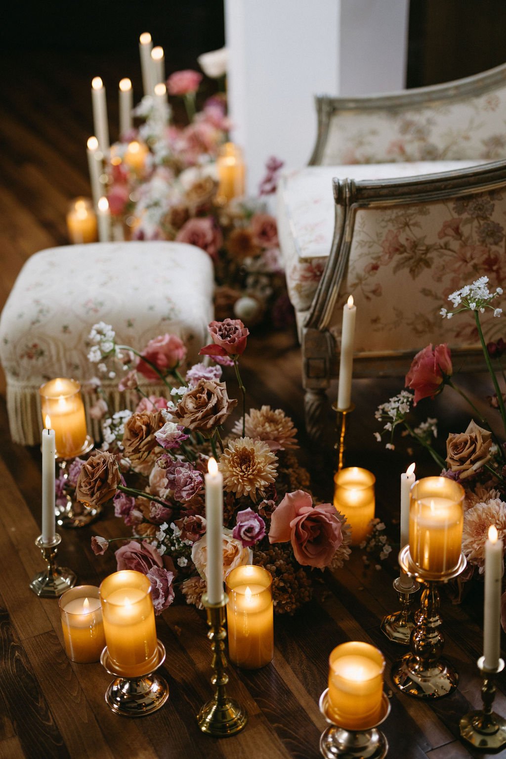 Antique floral upholstered armchair and ottoman accenting a lush floor floral display with warm pillar candles.   