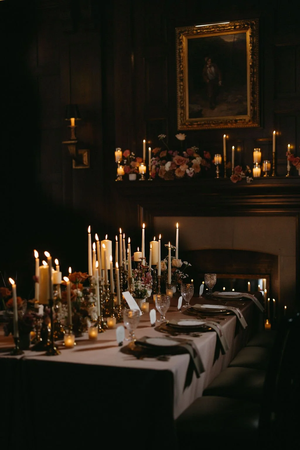 Candlelit wedding reception table featuring dozens of pillar candles, gold accents, and dark wood panelling.   